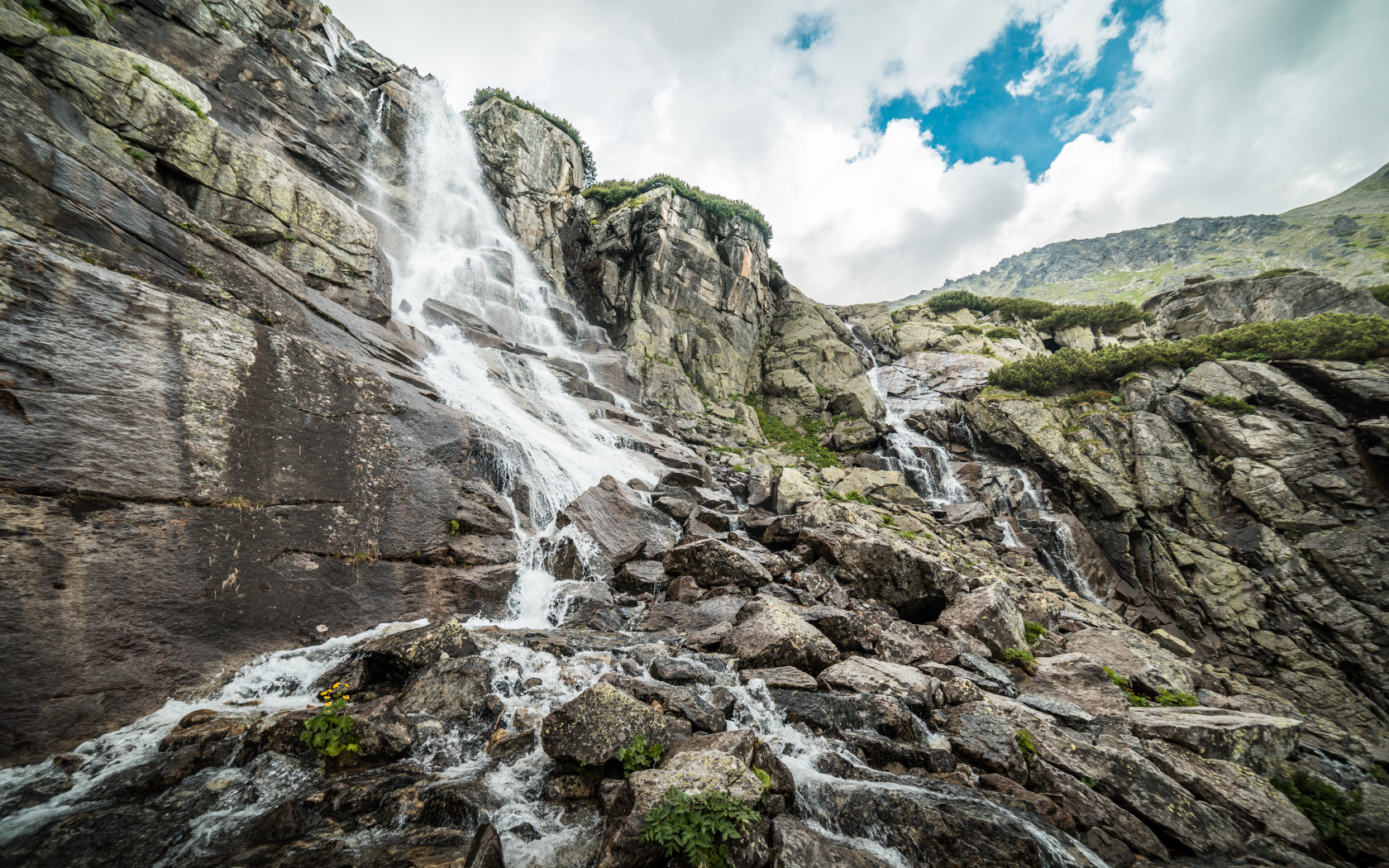 Водопад стекает по камням на фоне неба с белыми облаками