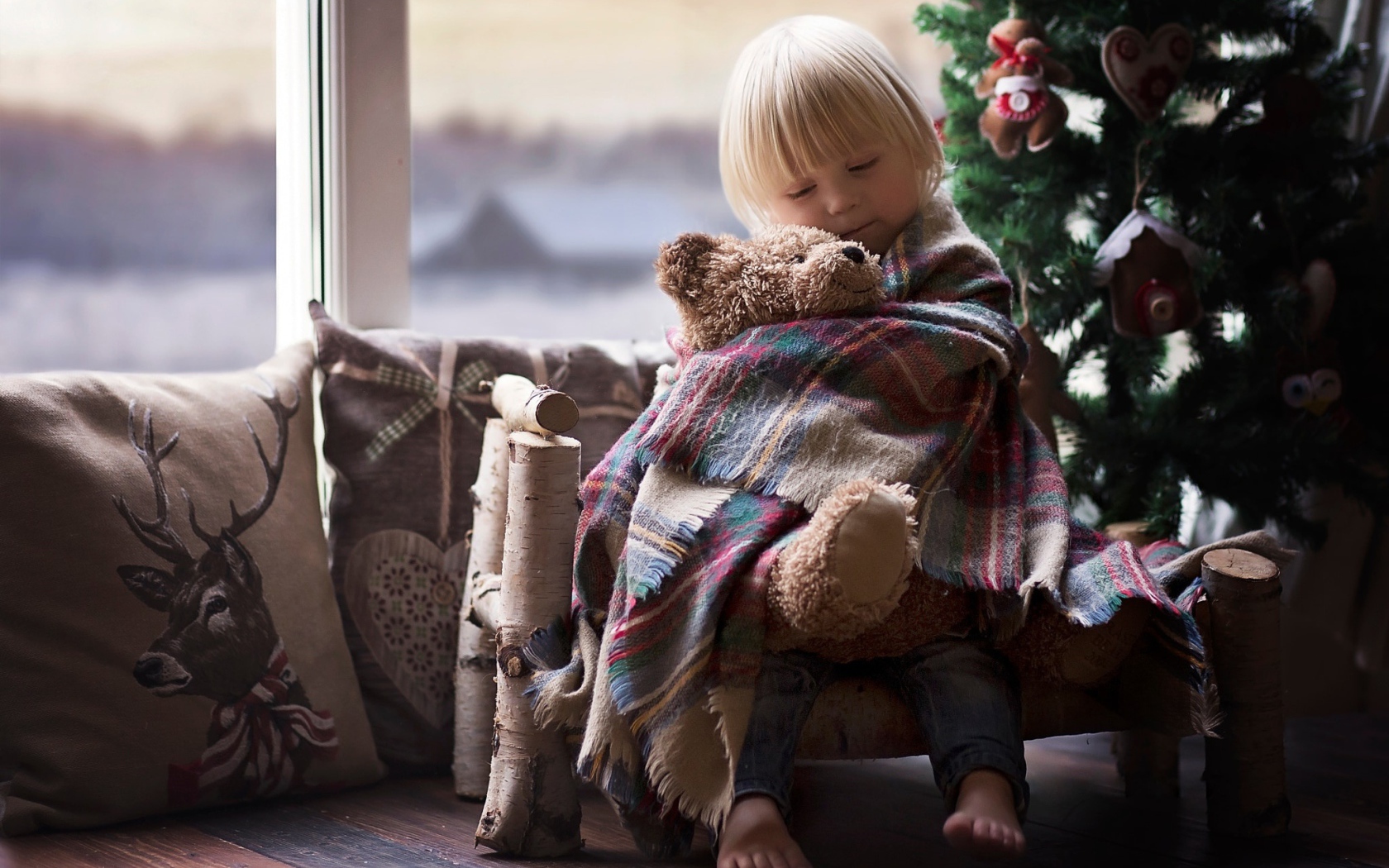 Маленькая девочка обнимает мишку у ели