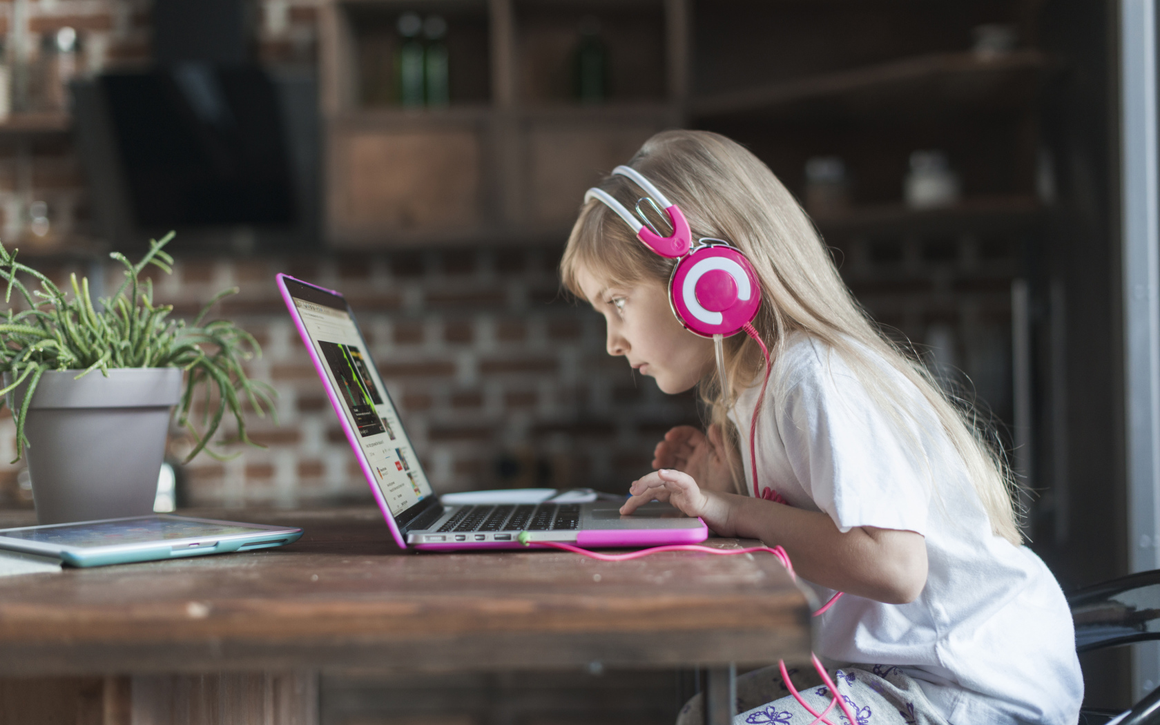 Маленькая девочка в наушниках сидит за ноутбуком