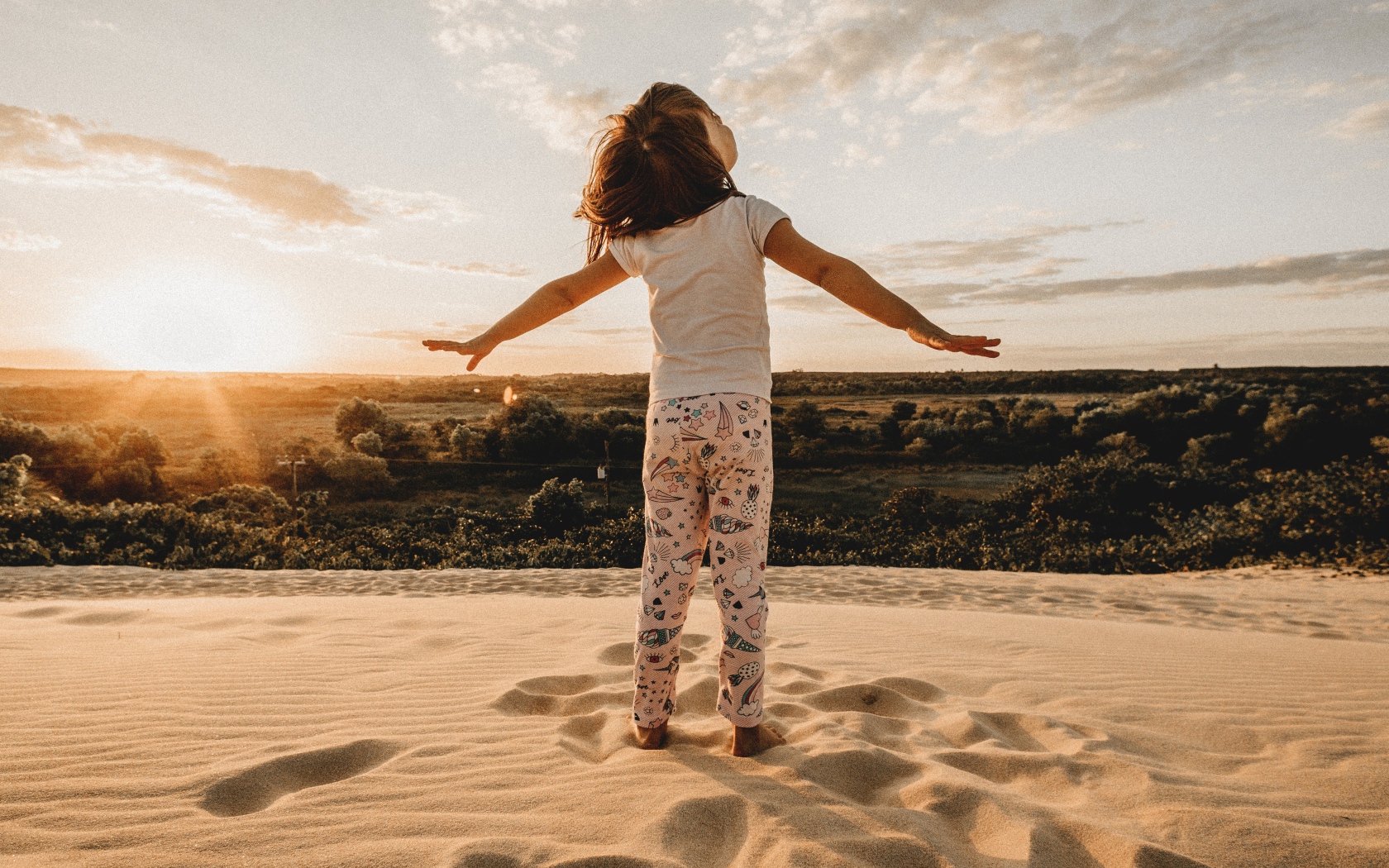 Маленькая девочка стоит на песку в лучах солнца