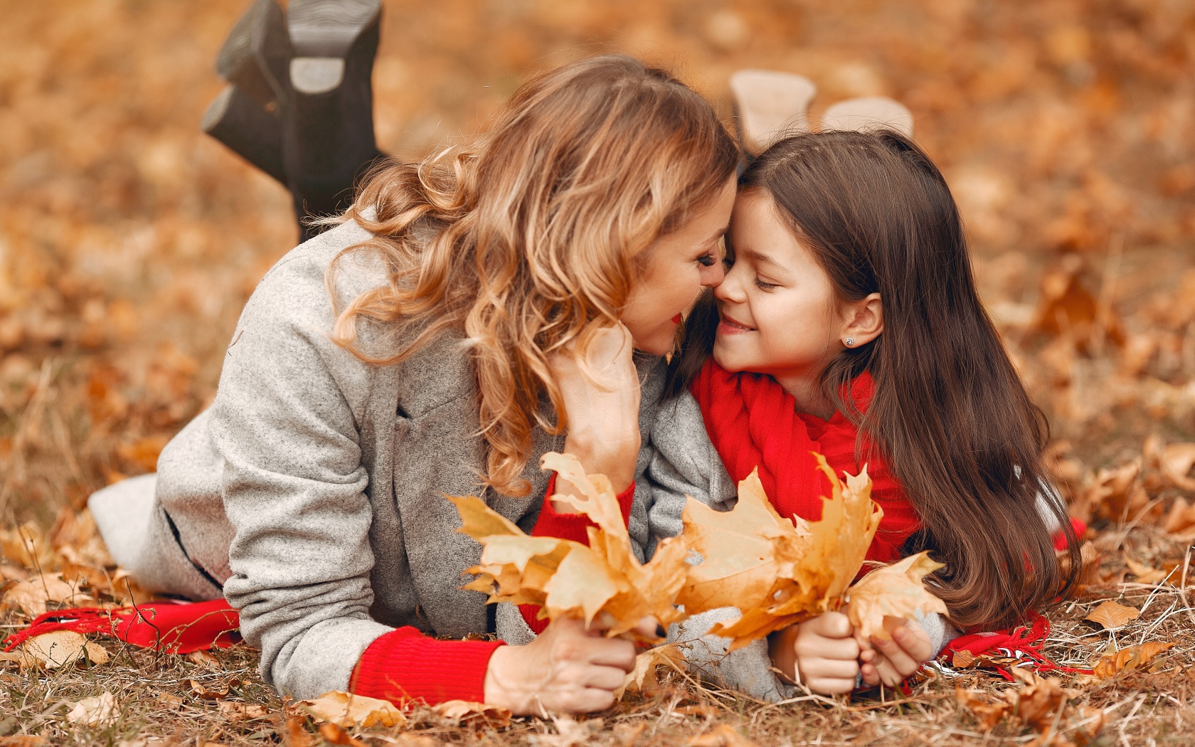 Мама с дочкой лежат на листве осенью 