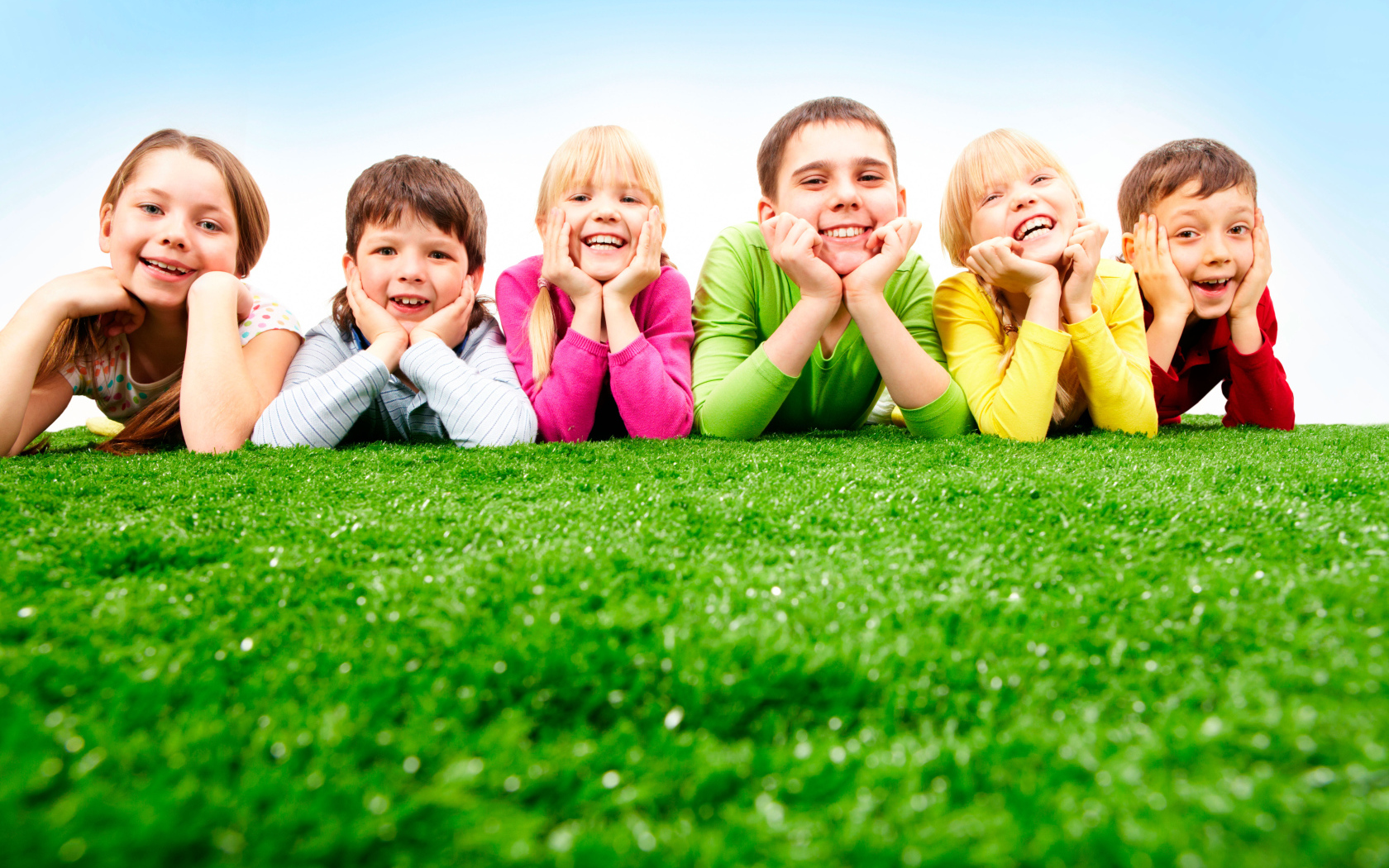 Улыбающиеся дети лежат на зеленой траве