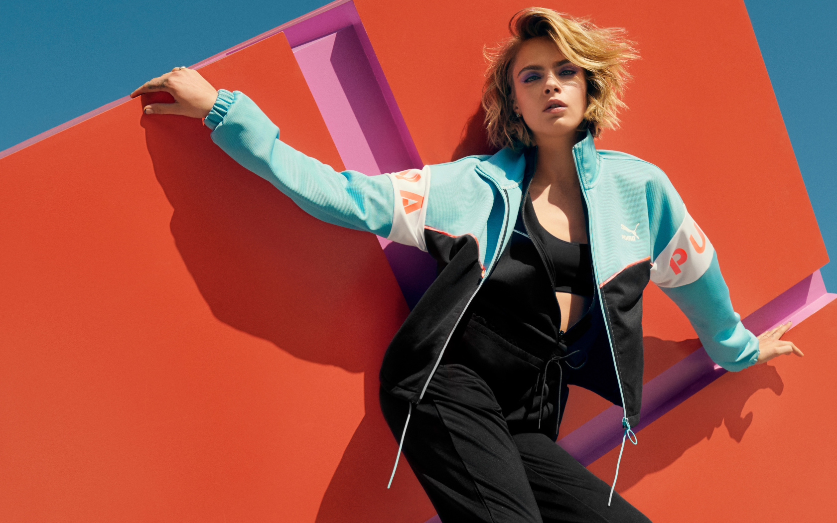 Красивая актриса Кара Делевинь в спортивном костюме у стены 