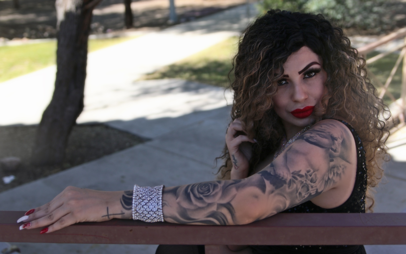 Красивая девушка с татуировками на руках сидит на лавке 