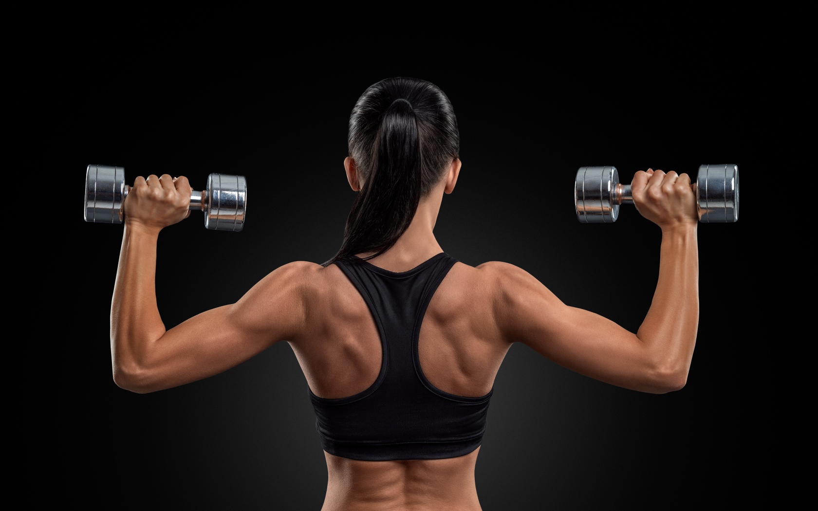 Стройная спортивная девушка с гантелями в руках на черном фоне
