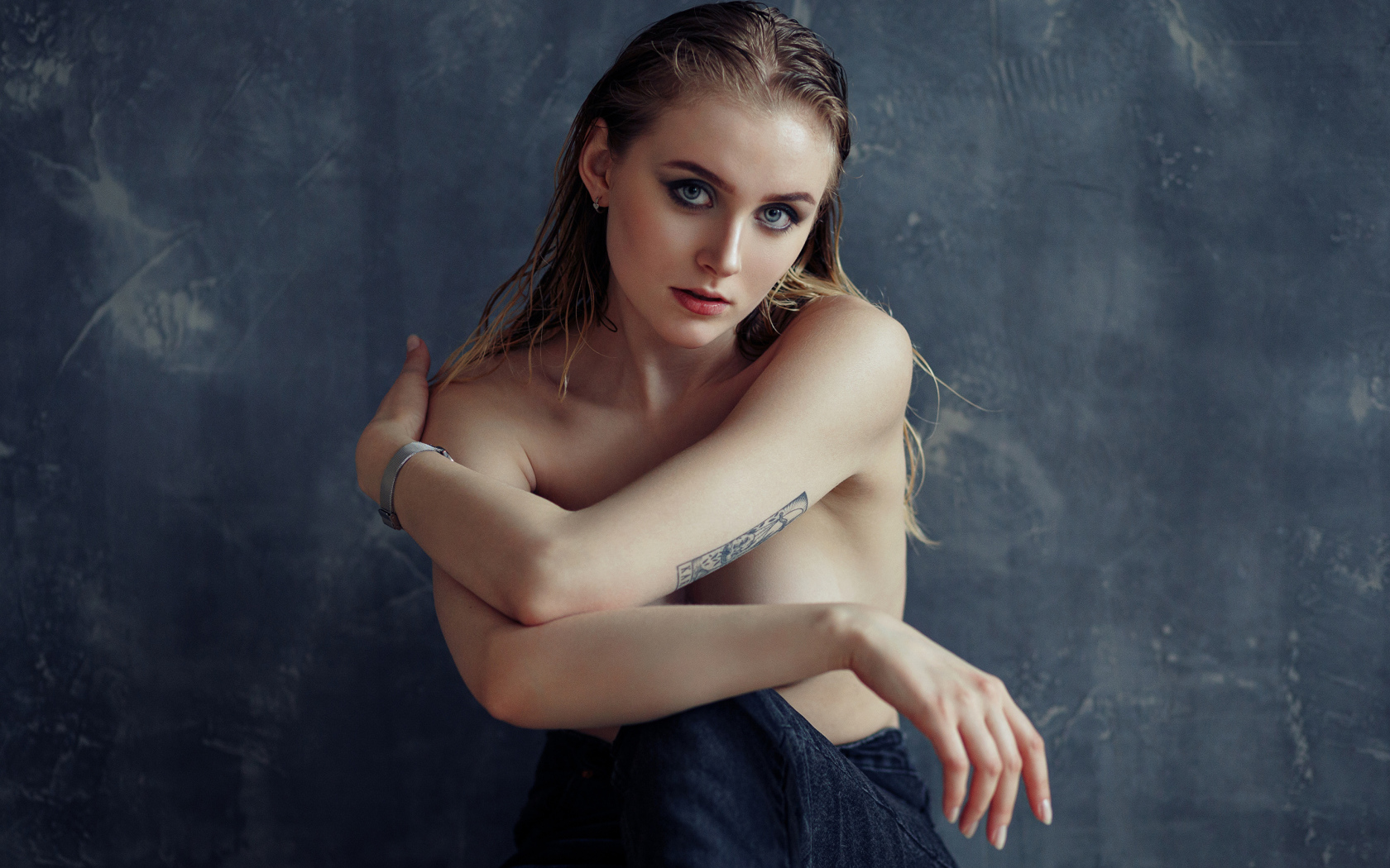 Нежная девушка с татуировками на теле сидит у стены