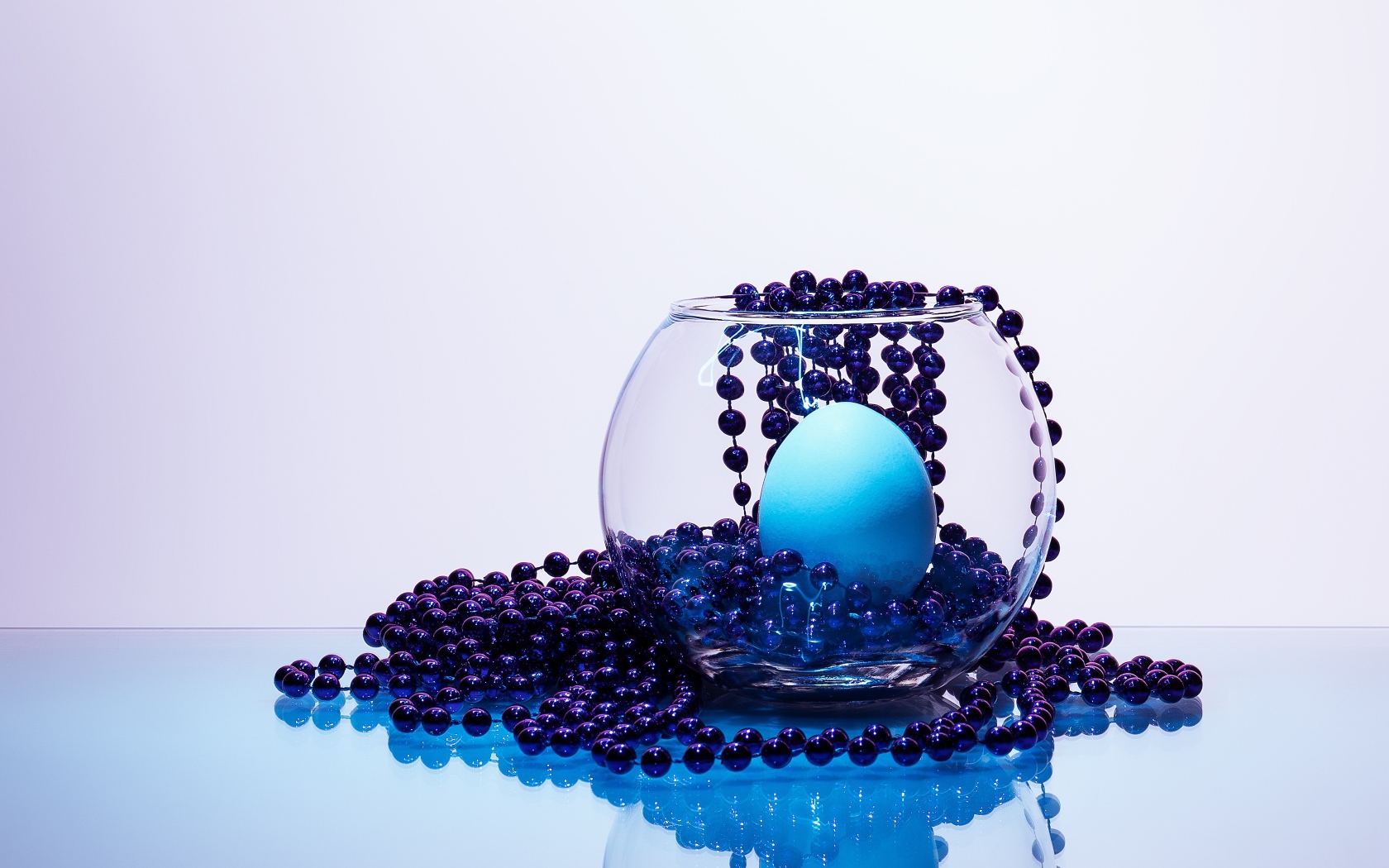 Синие бусы на столе со стеклянной вазой и яйцом