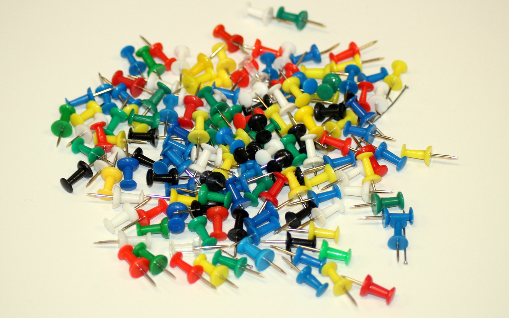 Разноцветные канцелярские гвозди на белом фоне
