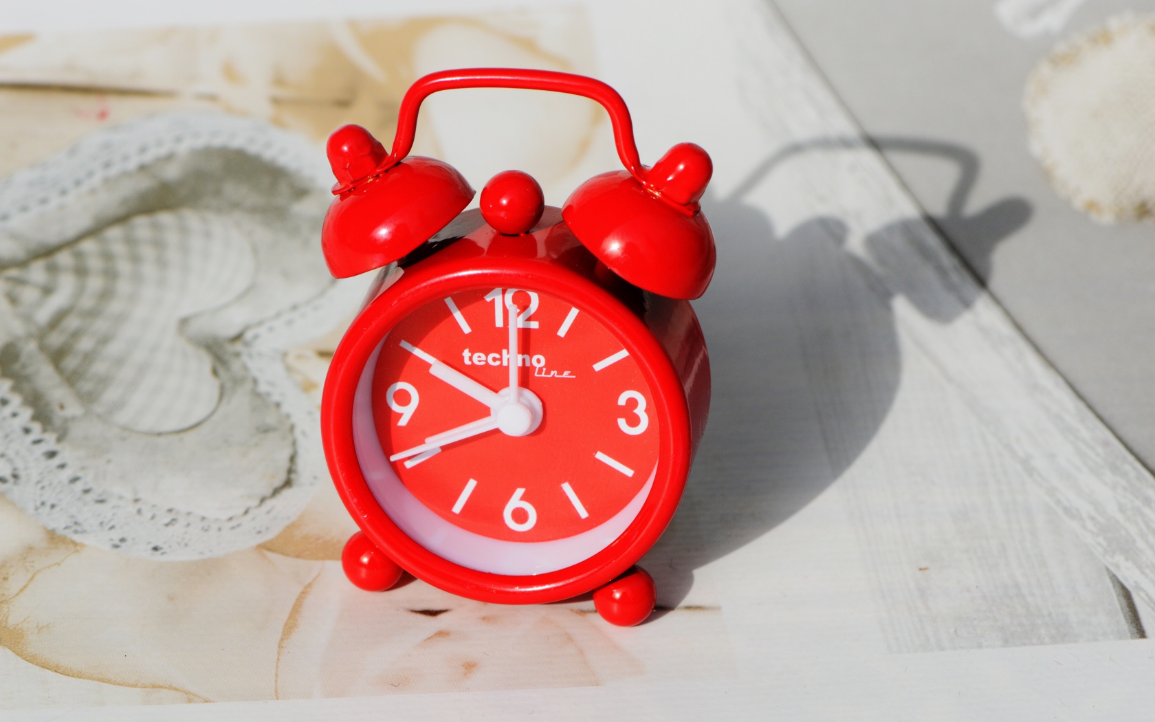 Маленький красный будильник стоит на столе 