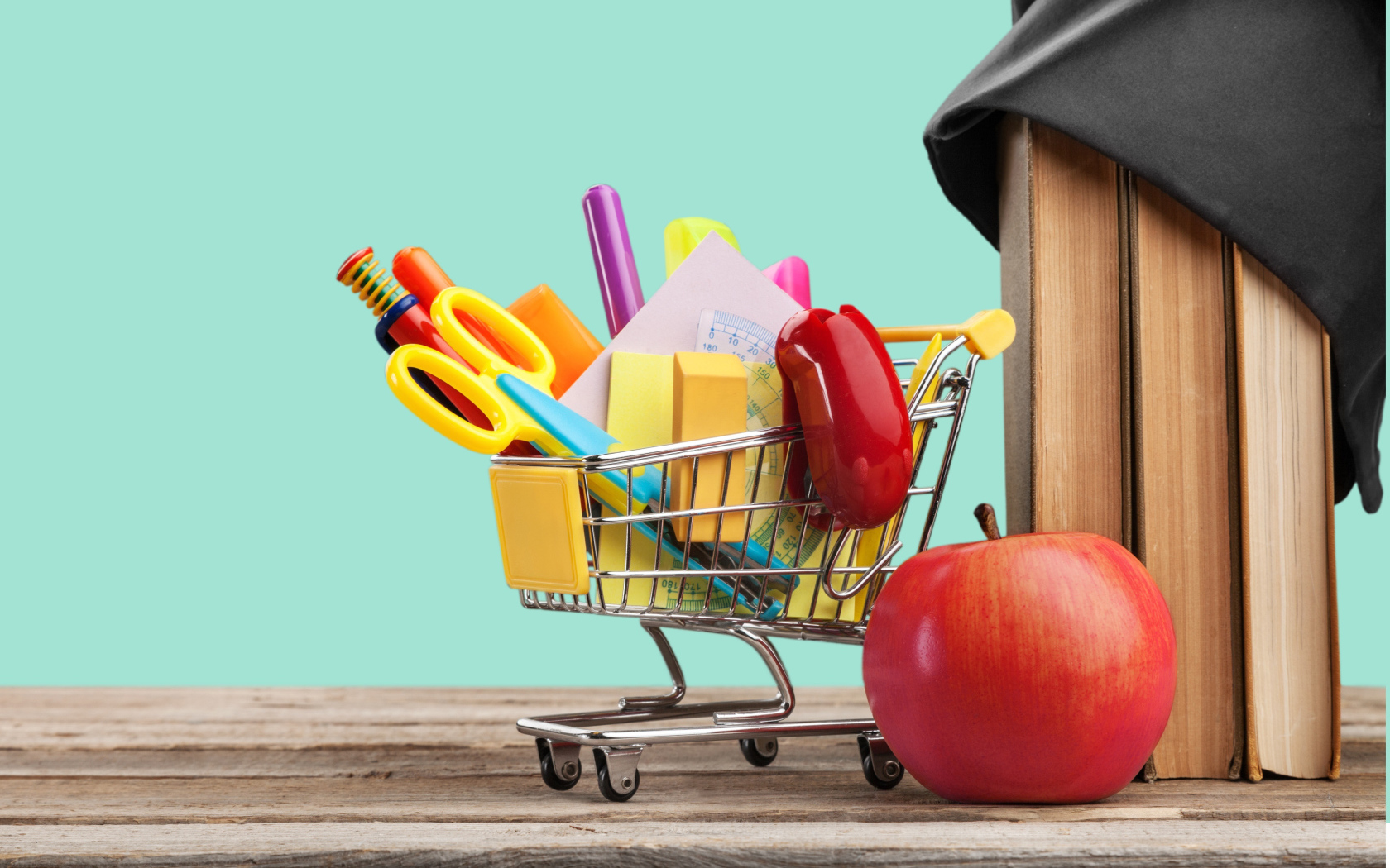 Канцелярские предметы в тележке на столе с яблоком и книгами 