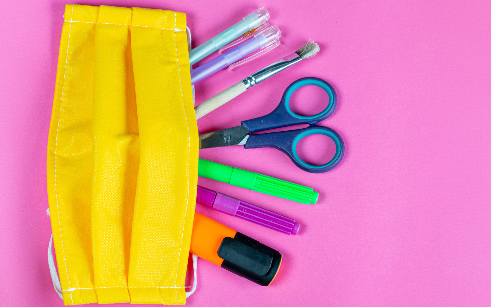 Желтая медицинская маска с ручками и ножницами на  розовом фоне