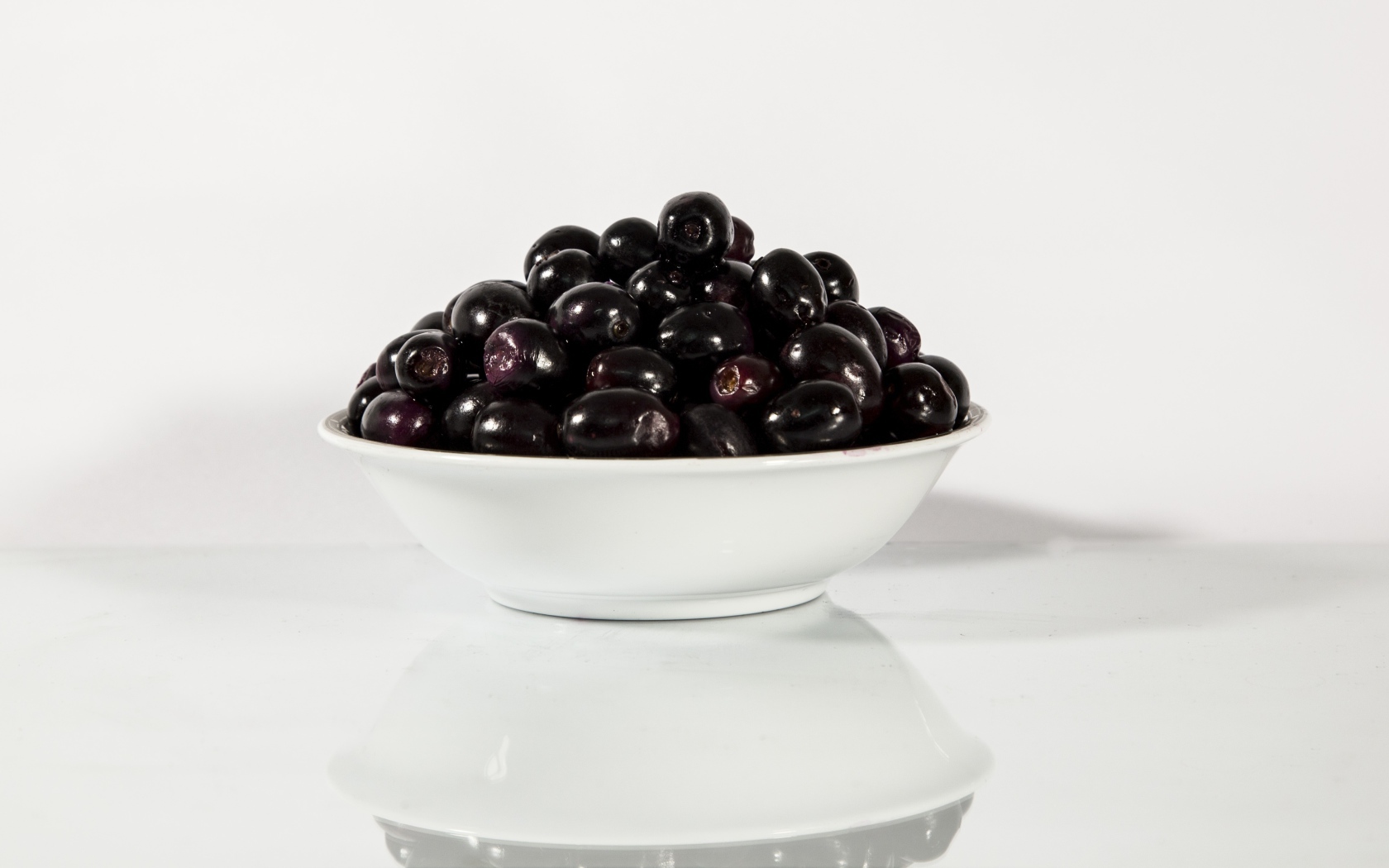 Черные оливки в белой тарелке отражаются в поверхности