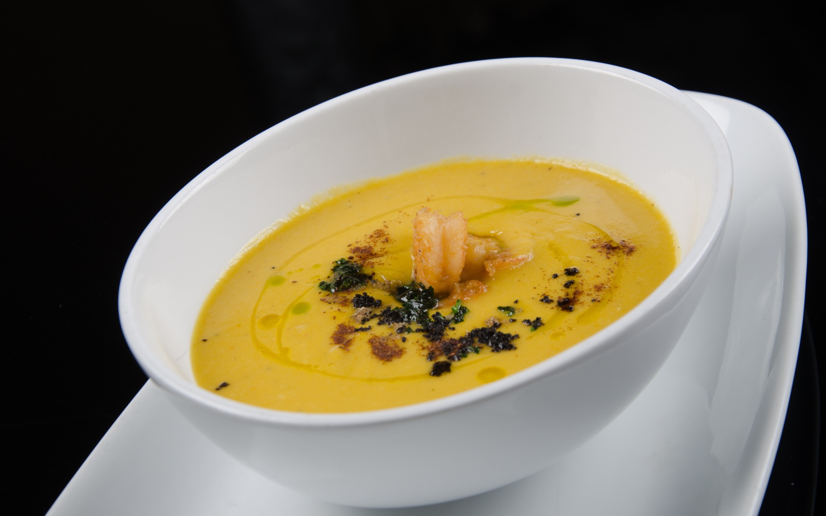 Желтый суп пюре в белой тарелке на черном фоне