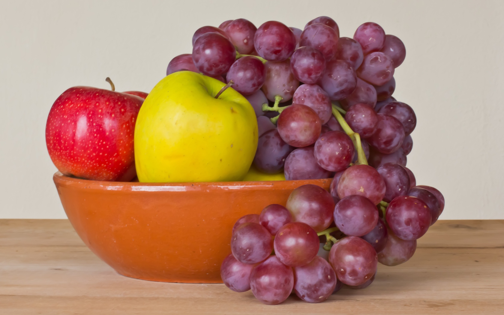 Яблоки и розовый виноград в тарелке на столе 