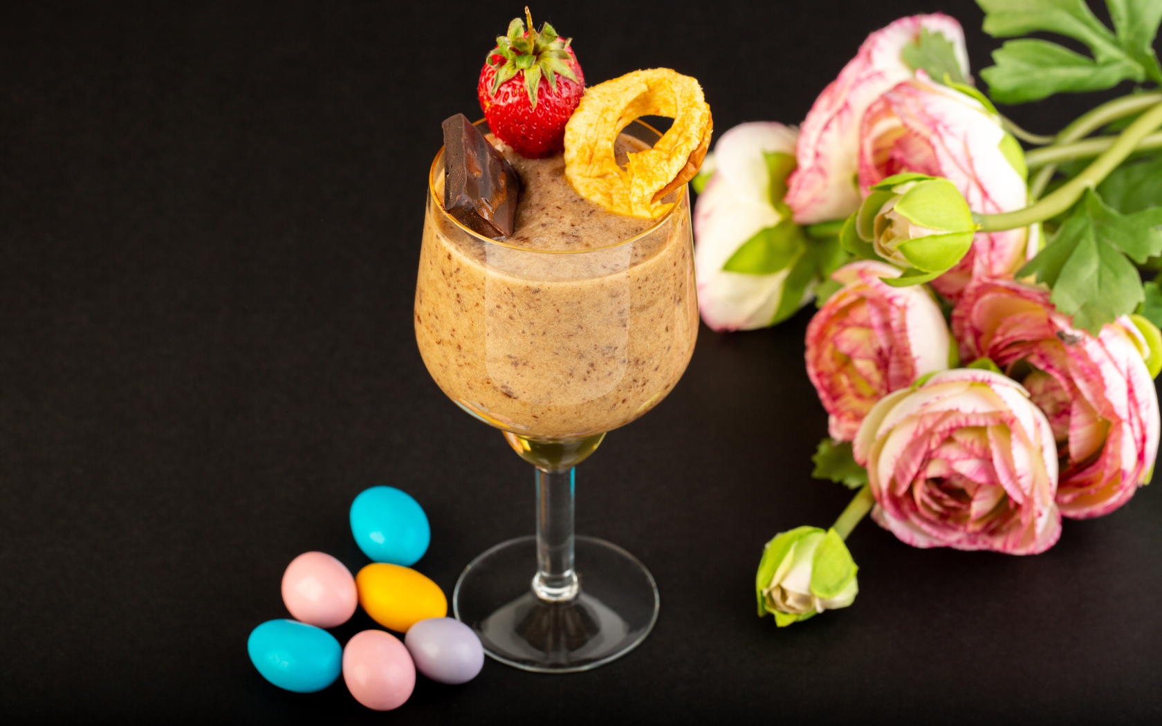 Коктейль с конфетами и букетом лютиков на черном столе