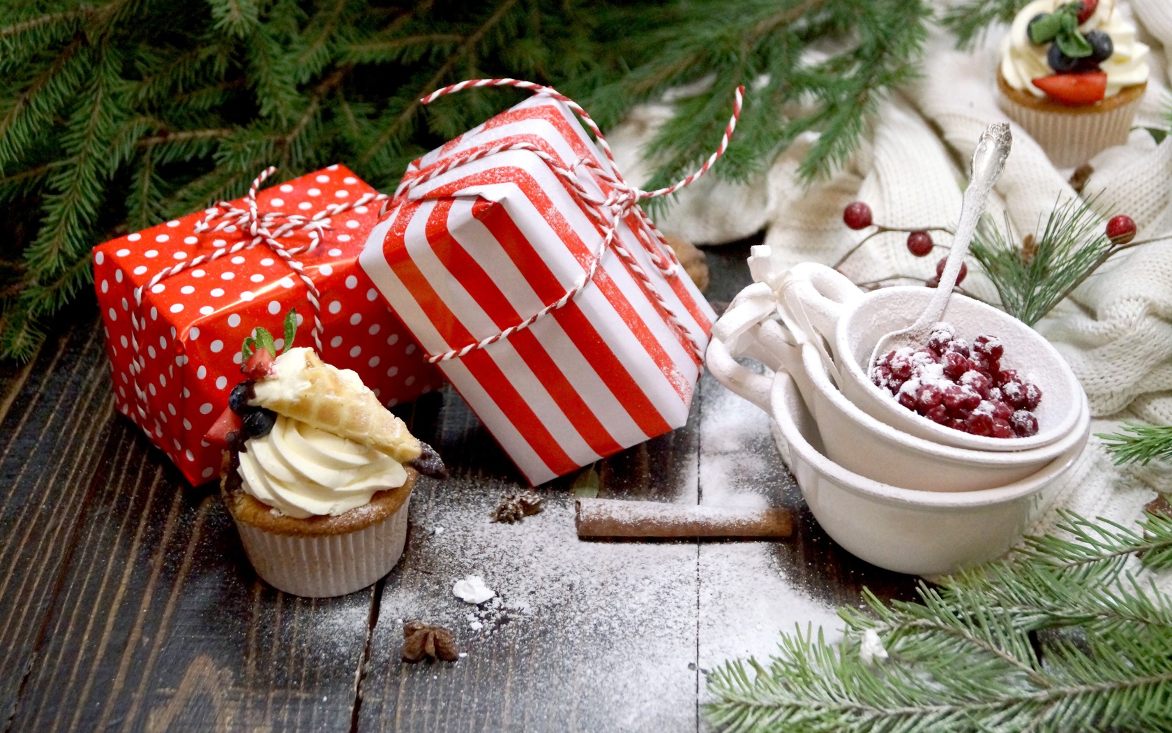 Два подарка на столе с еловой веткой и кексами 