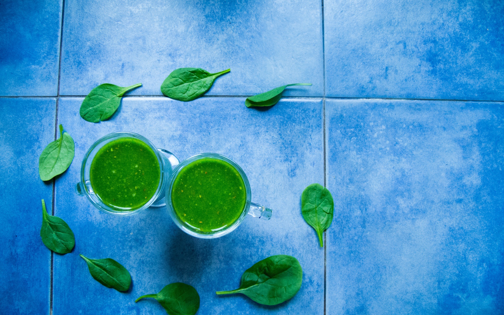 Два зеленых смузи с листьями базилика на голубом фоне