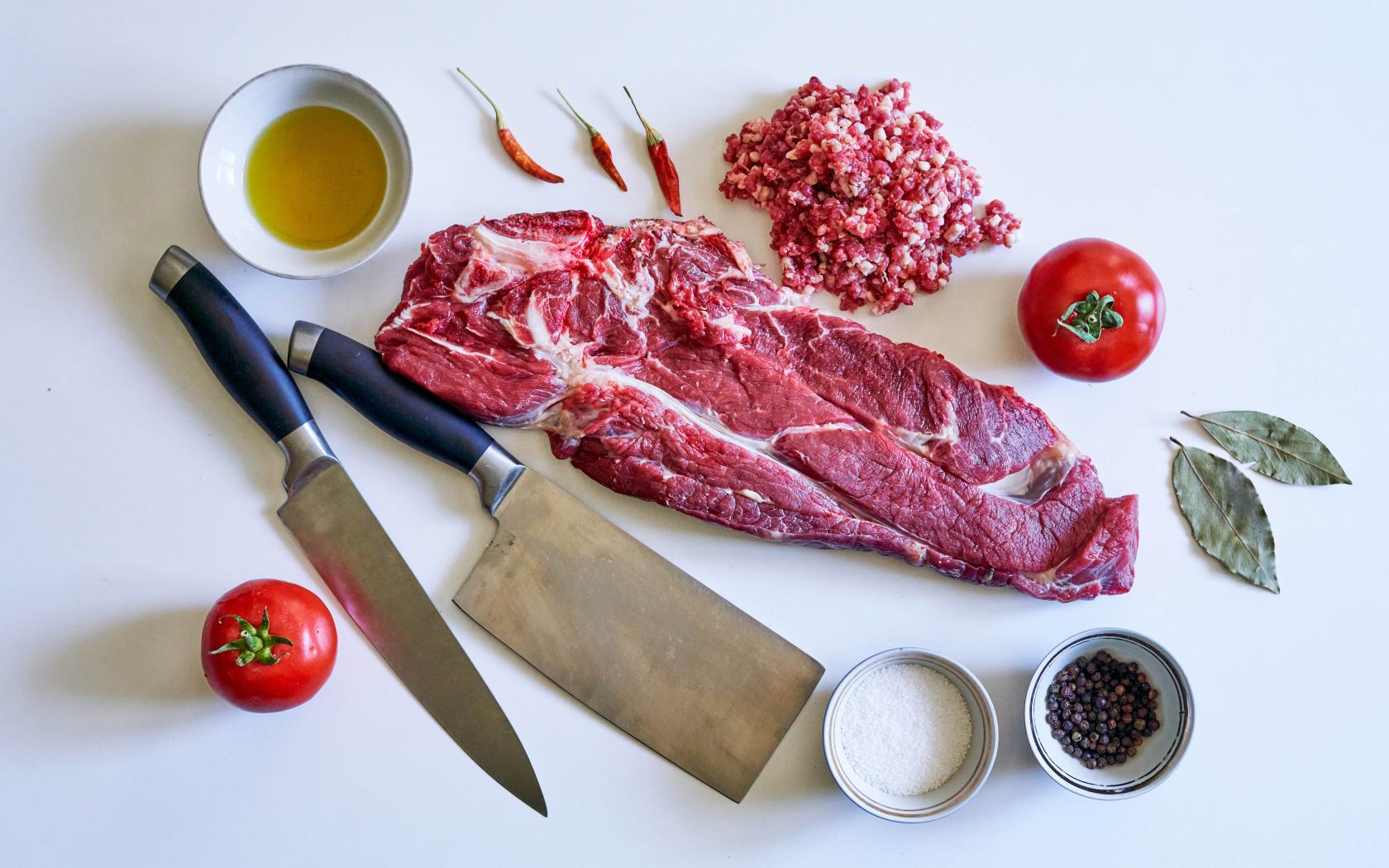 Кусок мяса со специями и ножами на столе 