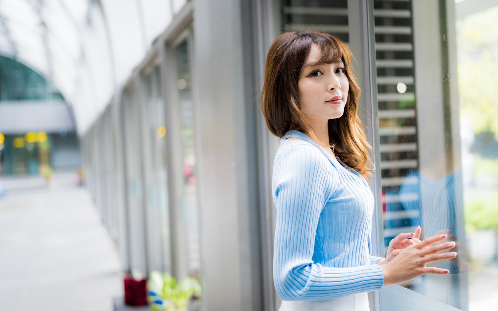 Красивая девушка азиатка в в голубой кофте стоит уокна