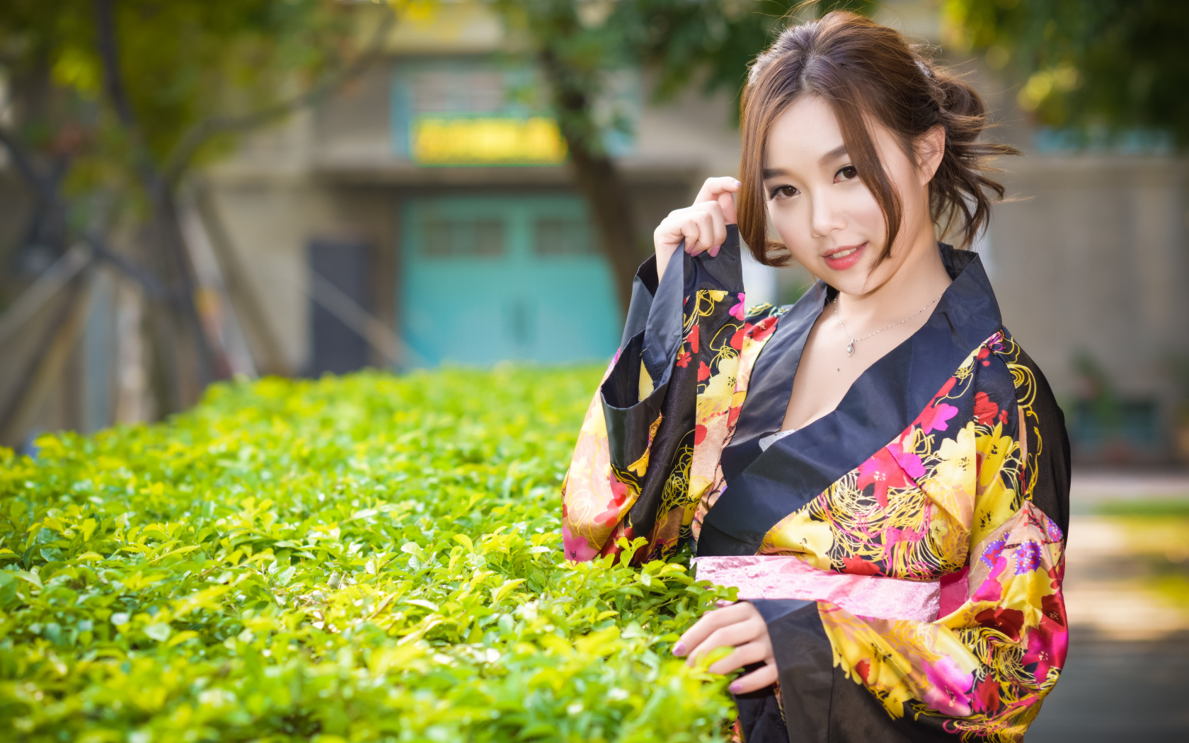 Девушка в кимоно стоит у зеленого куста