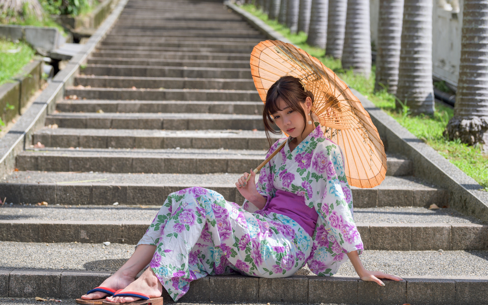 Девушка азиатка в кимоно с зонтом в руках сидит на ступеньках 