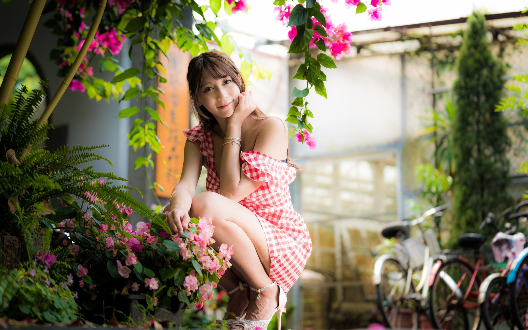 Девушка азиатка сидит на корточках у розового цветка