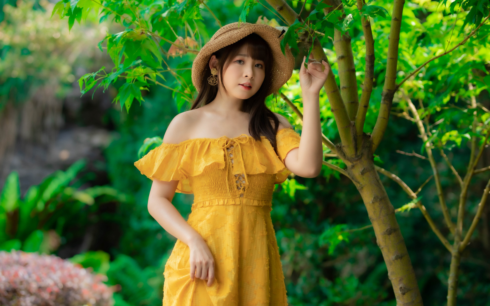 Красивая девушка азиатка в желтом платье   шляпе у дерева