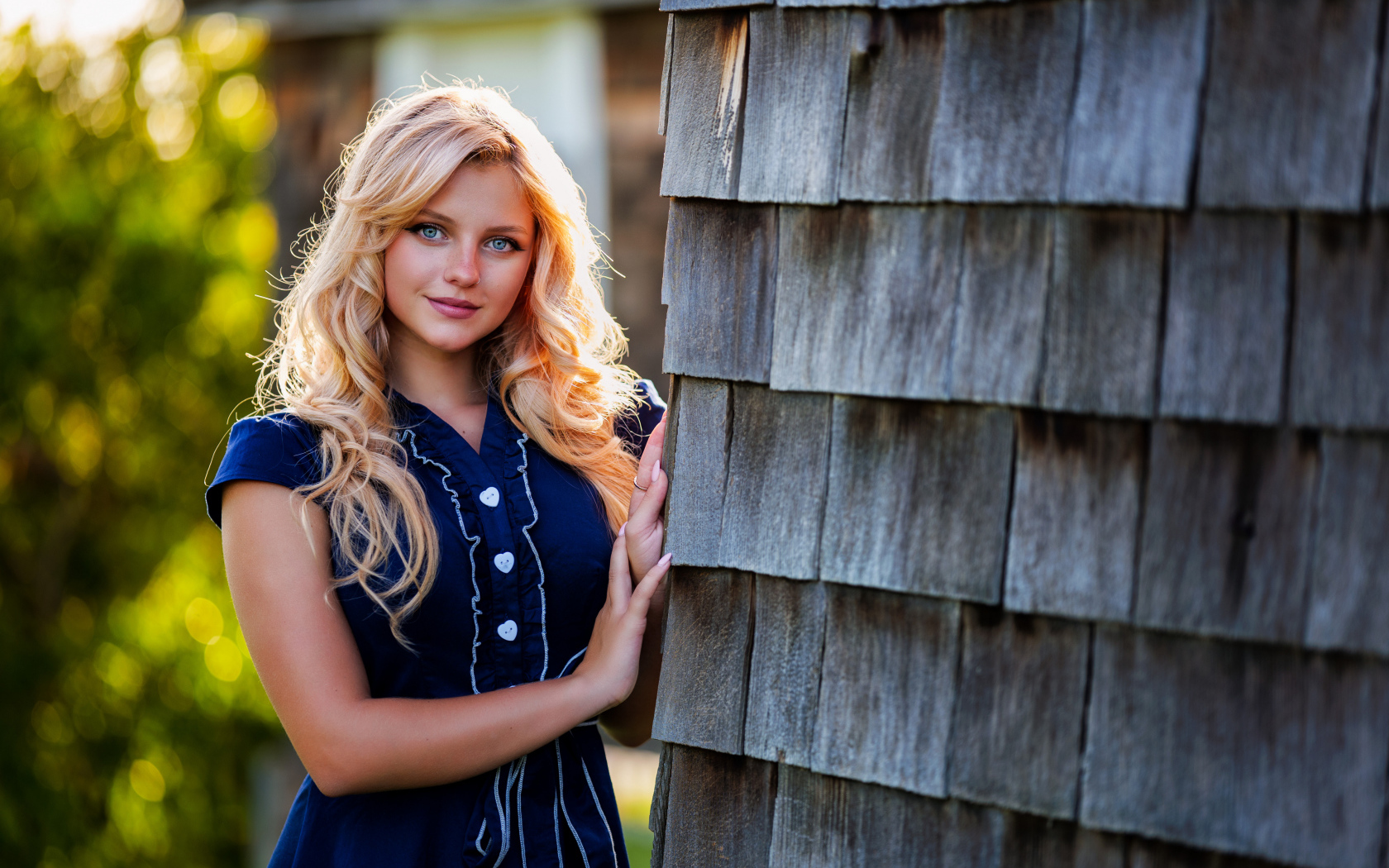 Голубоглазая блондинка в платье стоит у стены 