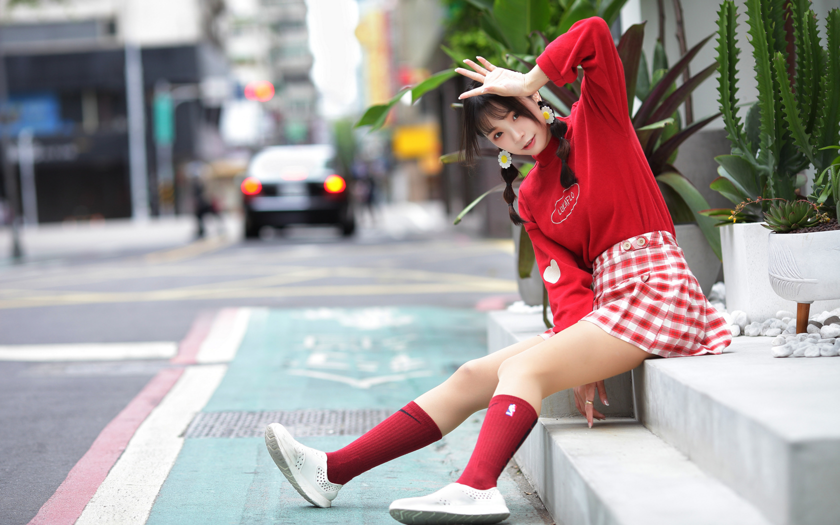 Веселая девушка азиатка в красном костюме сидит на ступеньках 