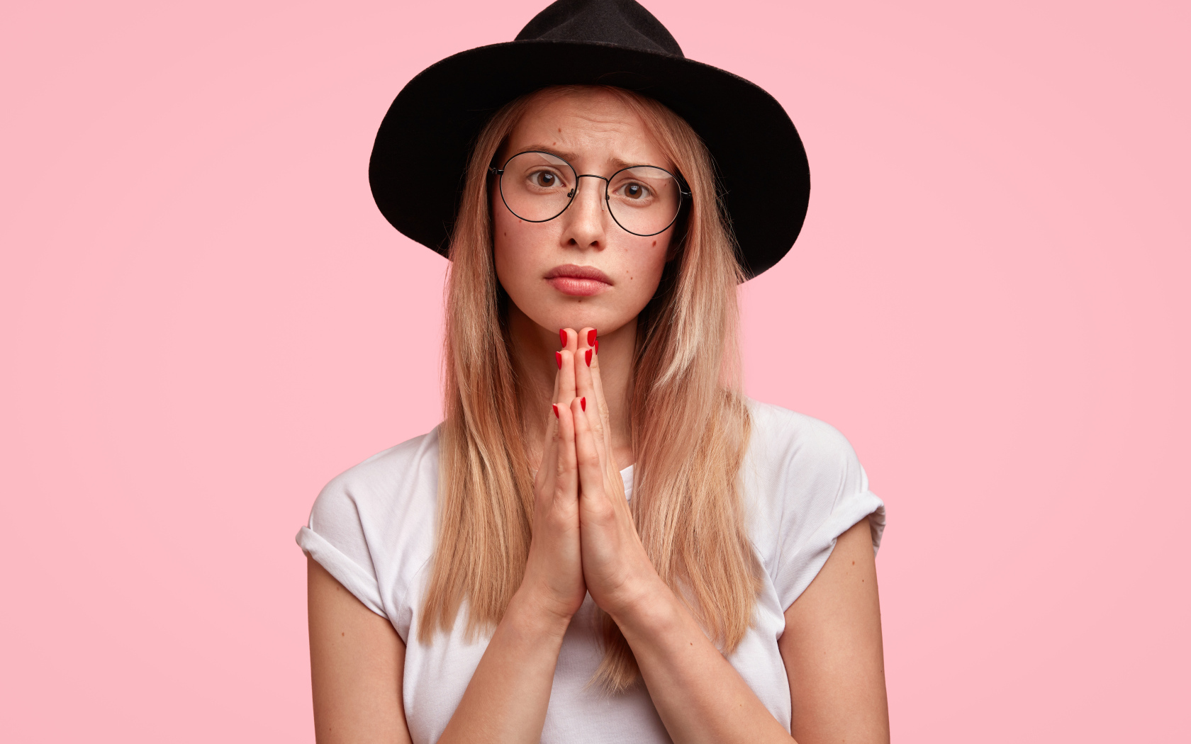 Девушка в черной шляпе на розовом фоне просит прощения