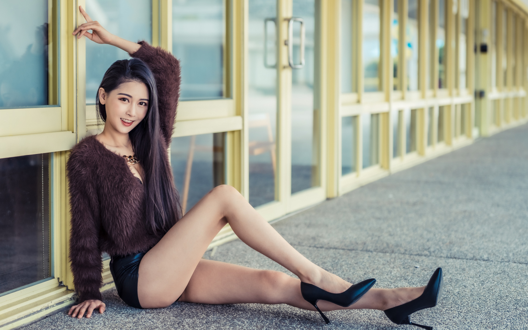 Девушка в свитере сидит у стеклянной стены 