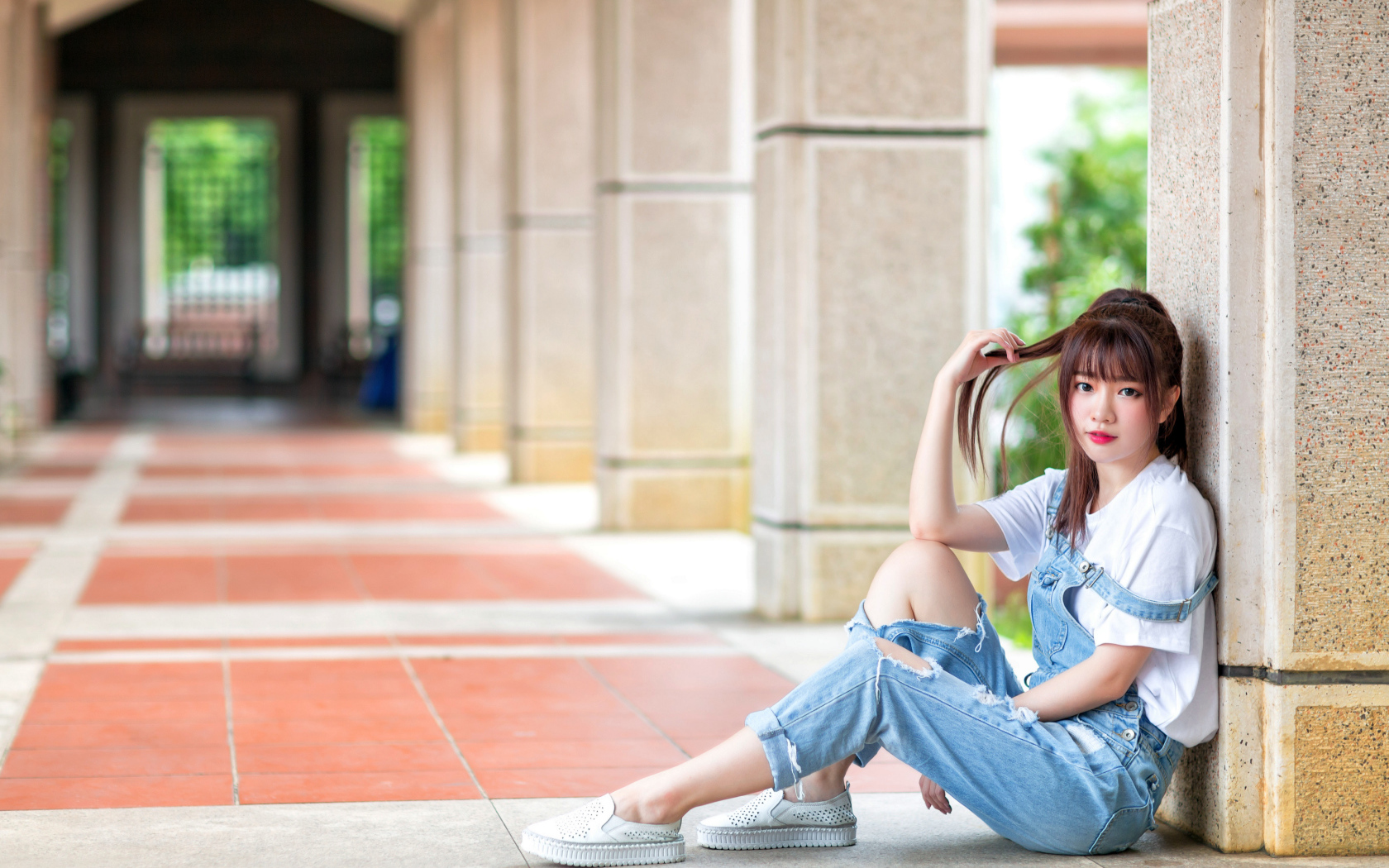 Грустная девушка азиатка сидит у колонны