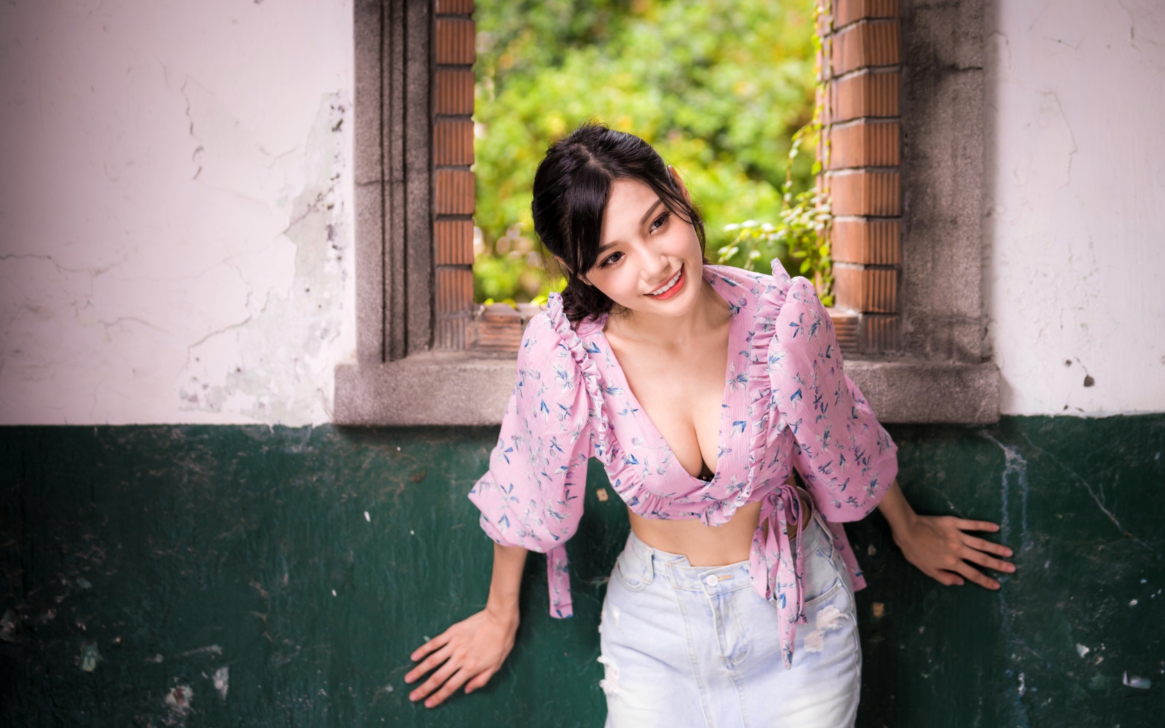 Улыбающаяся девушка азиатка стоит у окна 