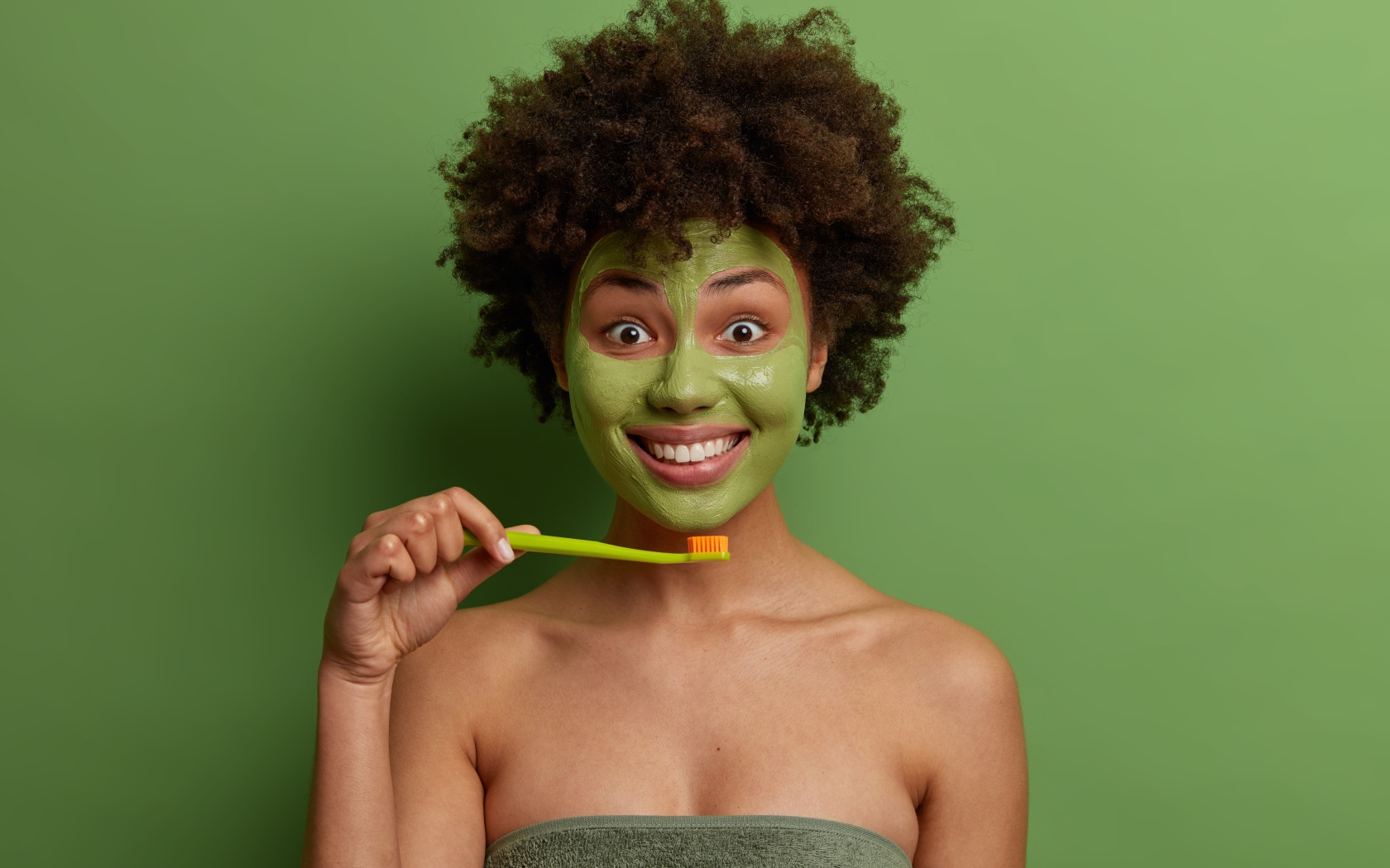 Улыбающаяся девушка с маской на лице чистит зубы