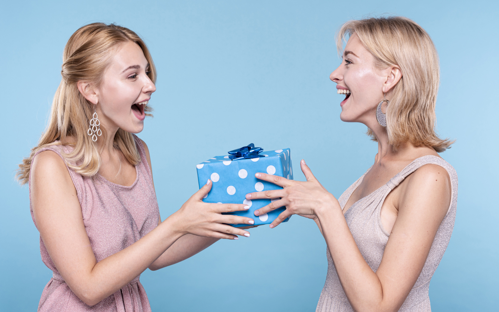 Две подруги блондинки с подарком на голубом фоне
