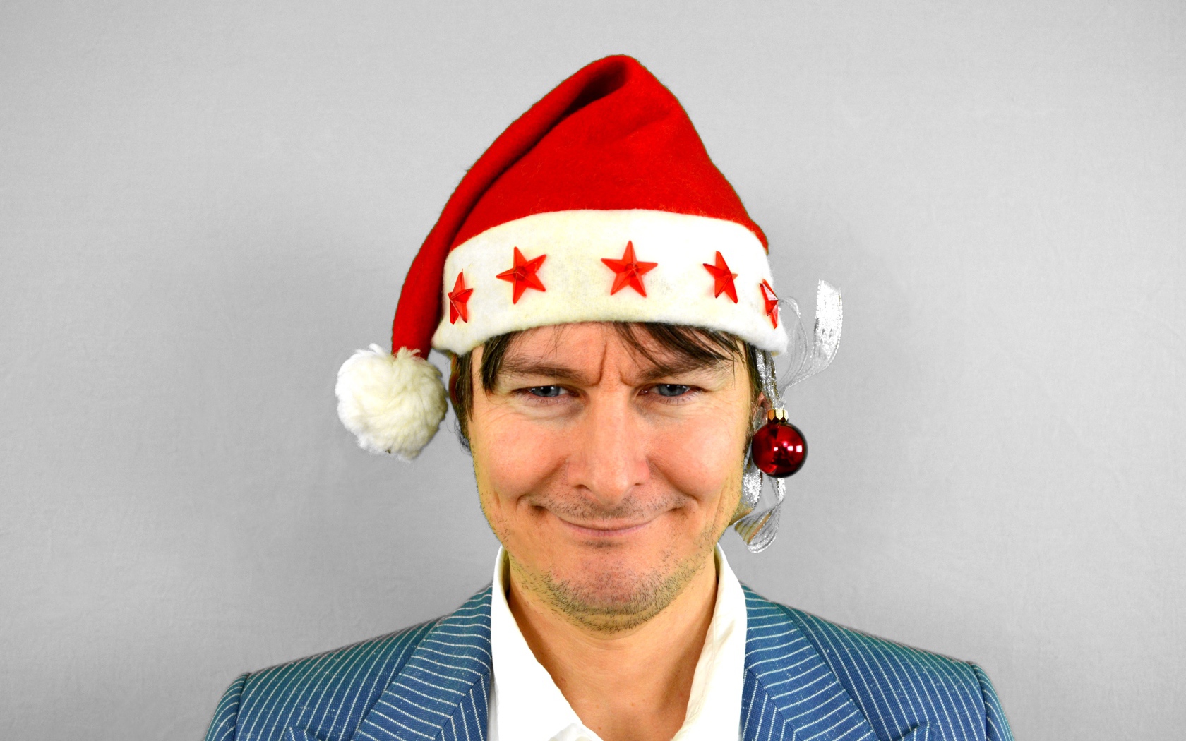 Голубоглазый мужчина в новогодней шапке на сером фоне 