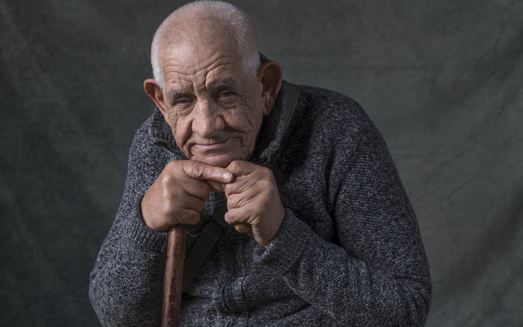 Пожилой мужчина в теплом свитере на сером фоне 