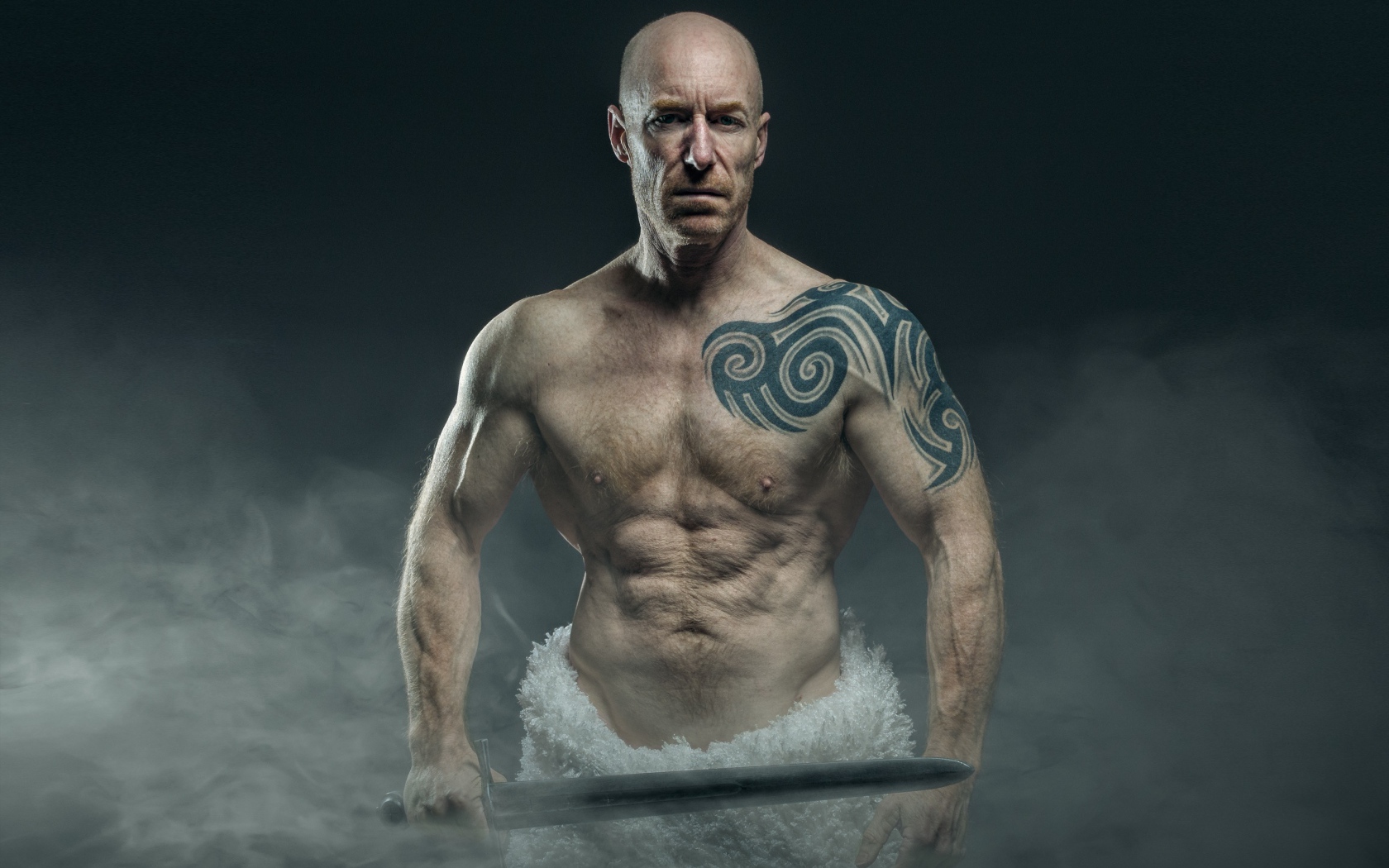 Сильный мужчина с мечом с татуировками на теле 