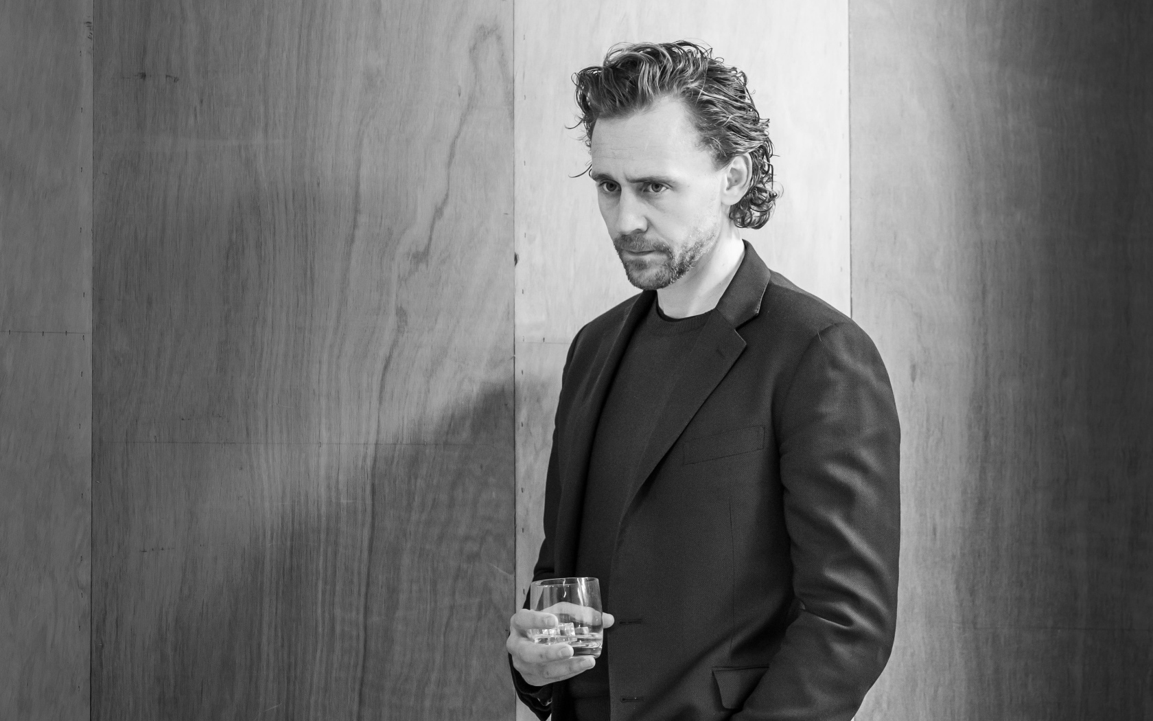 Актер Том Хиддлстон с бокалом в руке на фоне стены