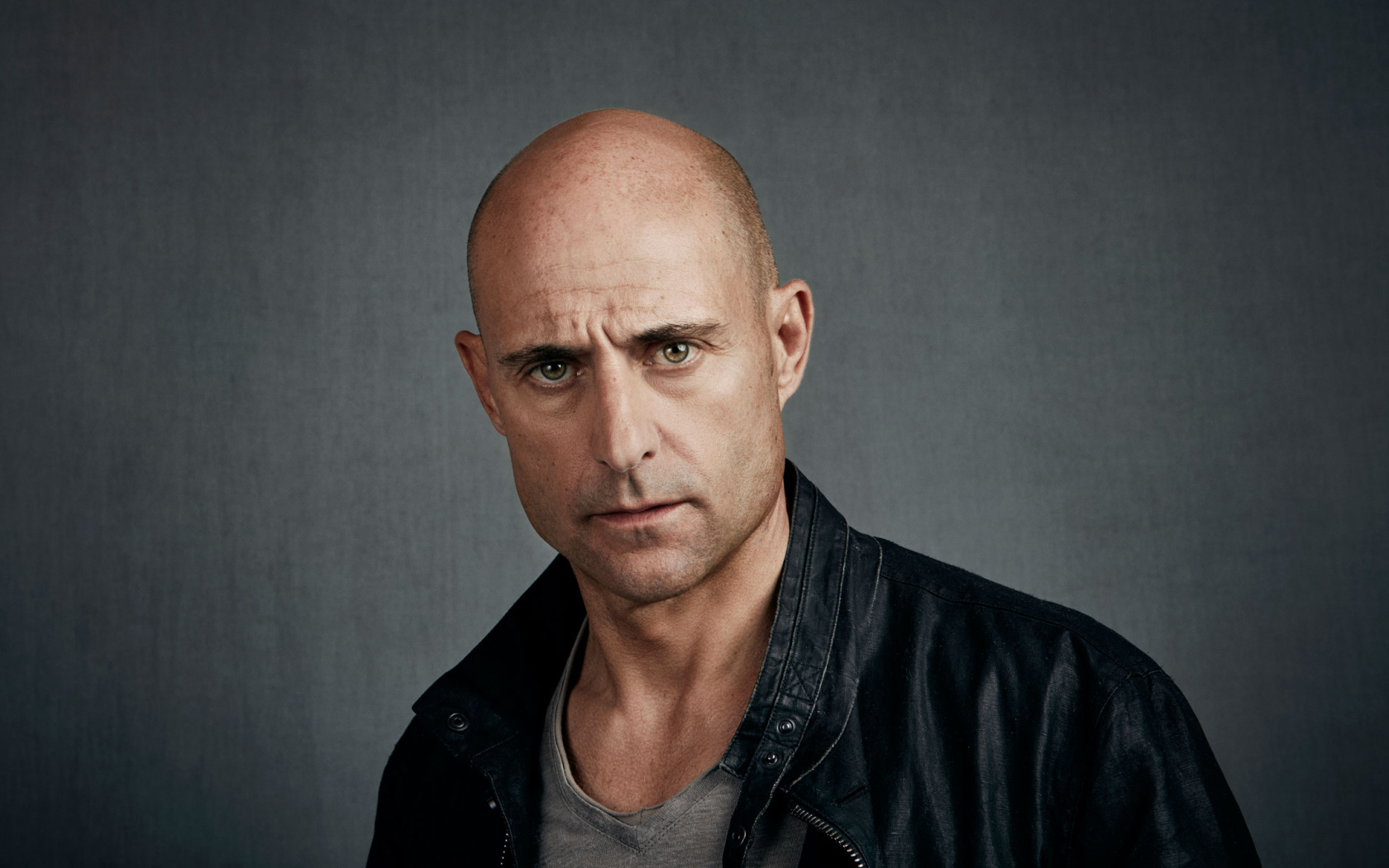 Марк Стронг в черной куртке на сером фоне