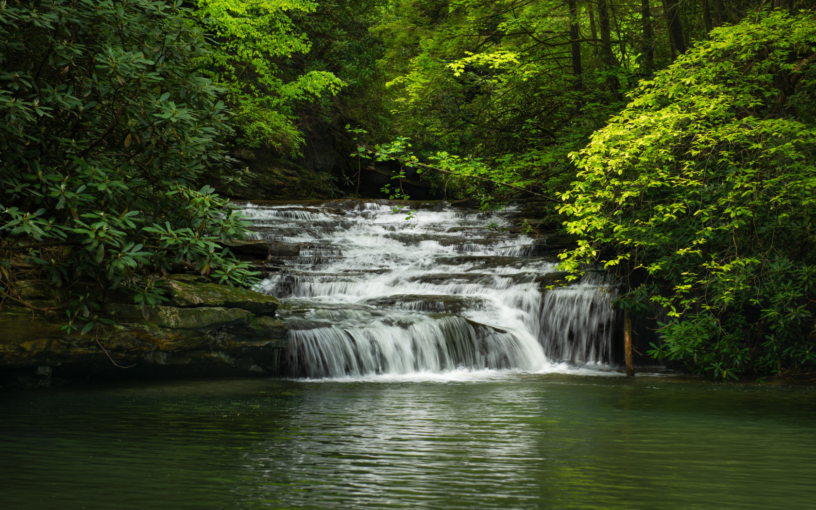 Водопад стекает по каменному каскаду в реку 