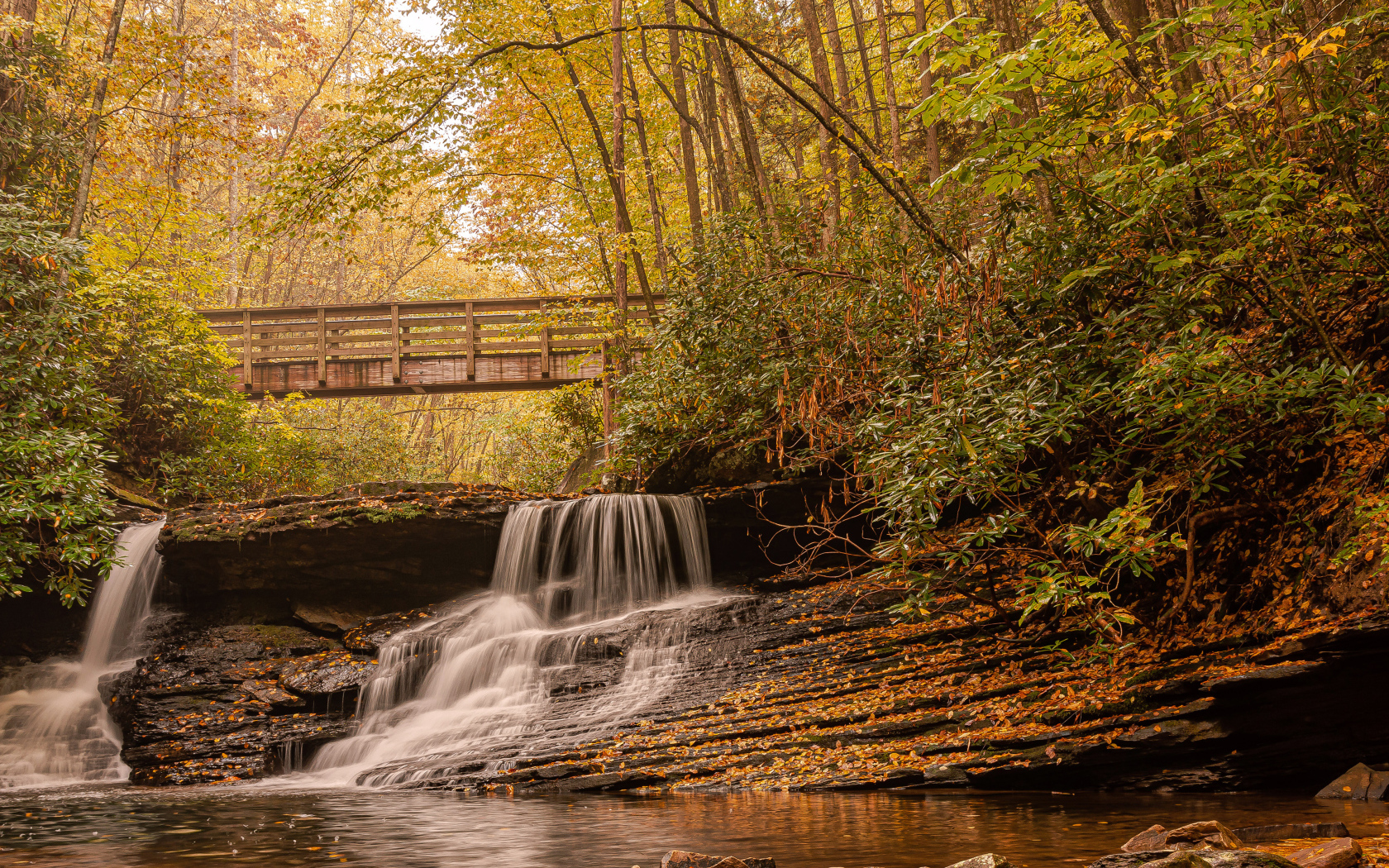 Водопад стекает по камням под мостом осенью