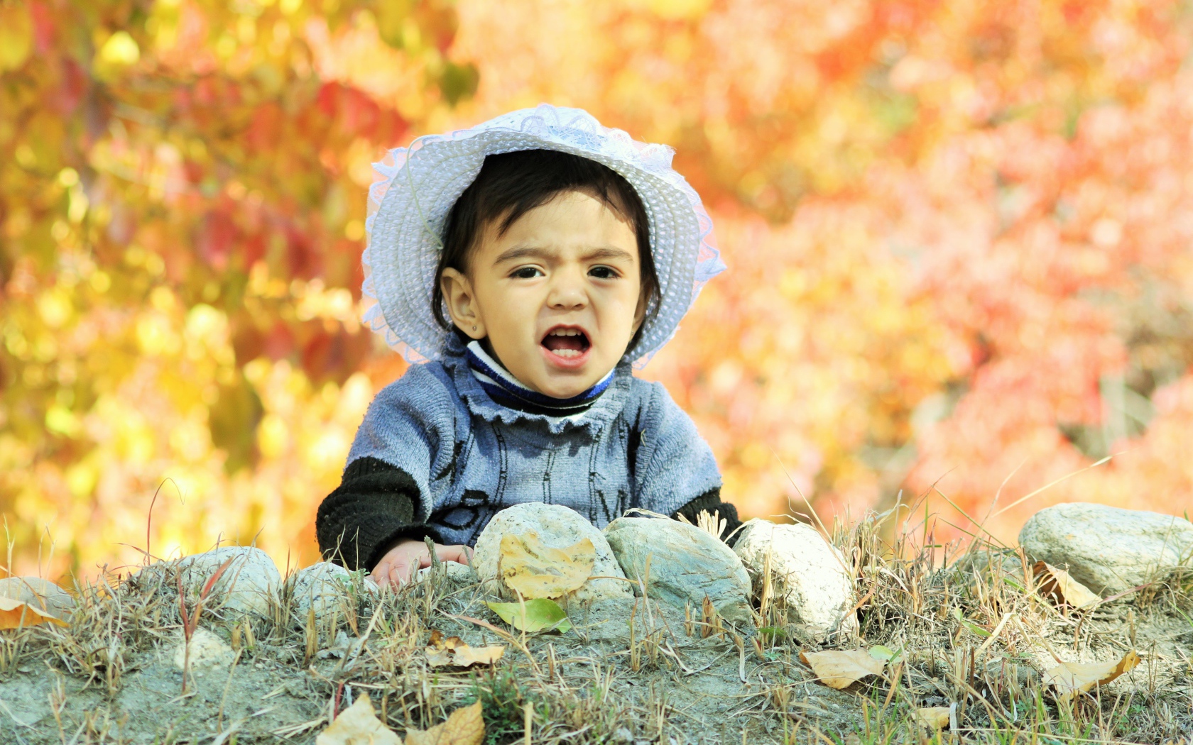 Маленькая девочка в шляпке сидит на земле