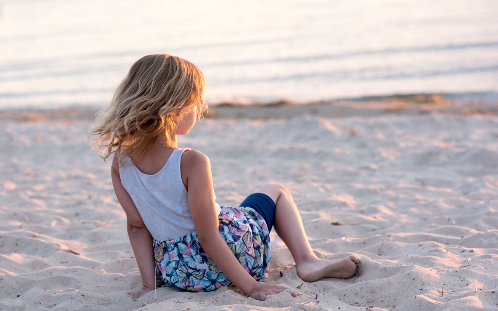 Маленькая девочка лежит на песке на закате 