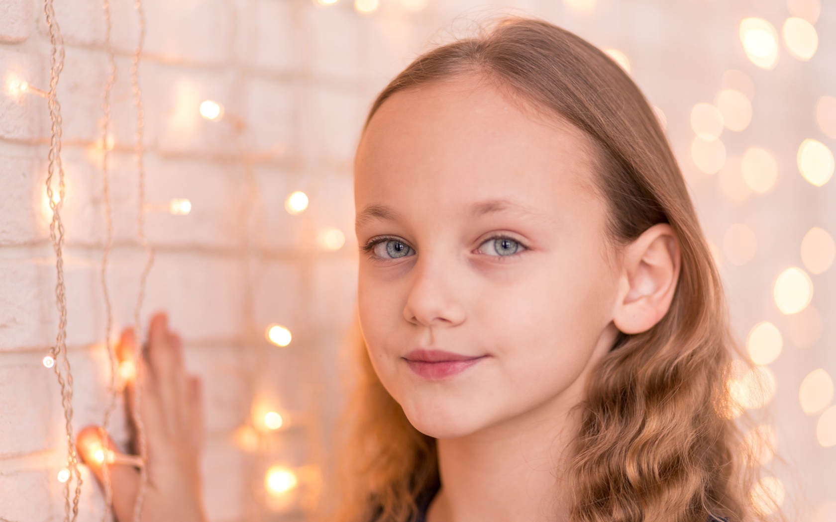 Красивая голубоглазая девочка стоит у стены с гирляндой