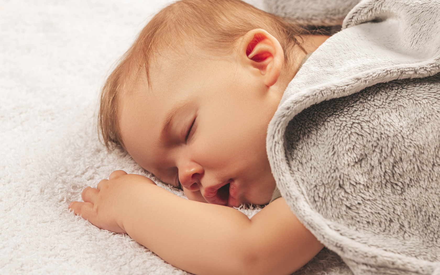 Маленький спящий ребенок под серым покрывалом 