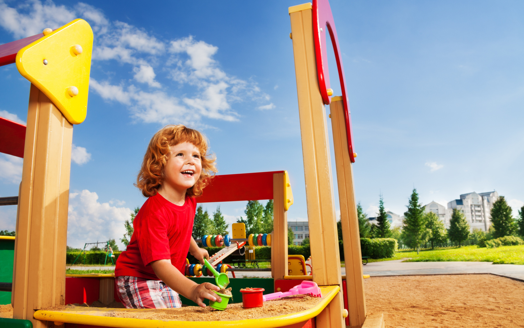 Улыбающийся мальчик в песочнице на детской площадке 