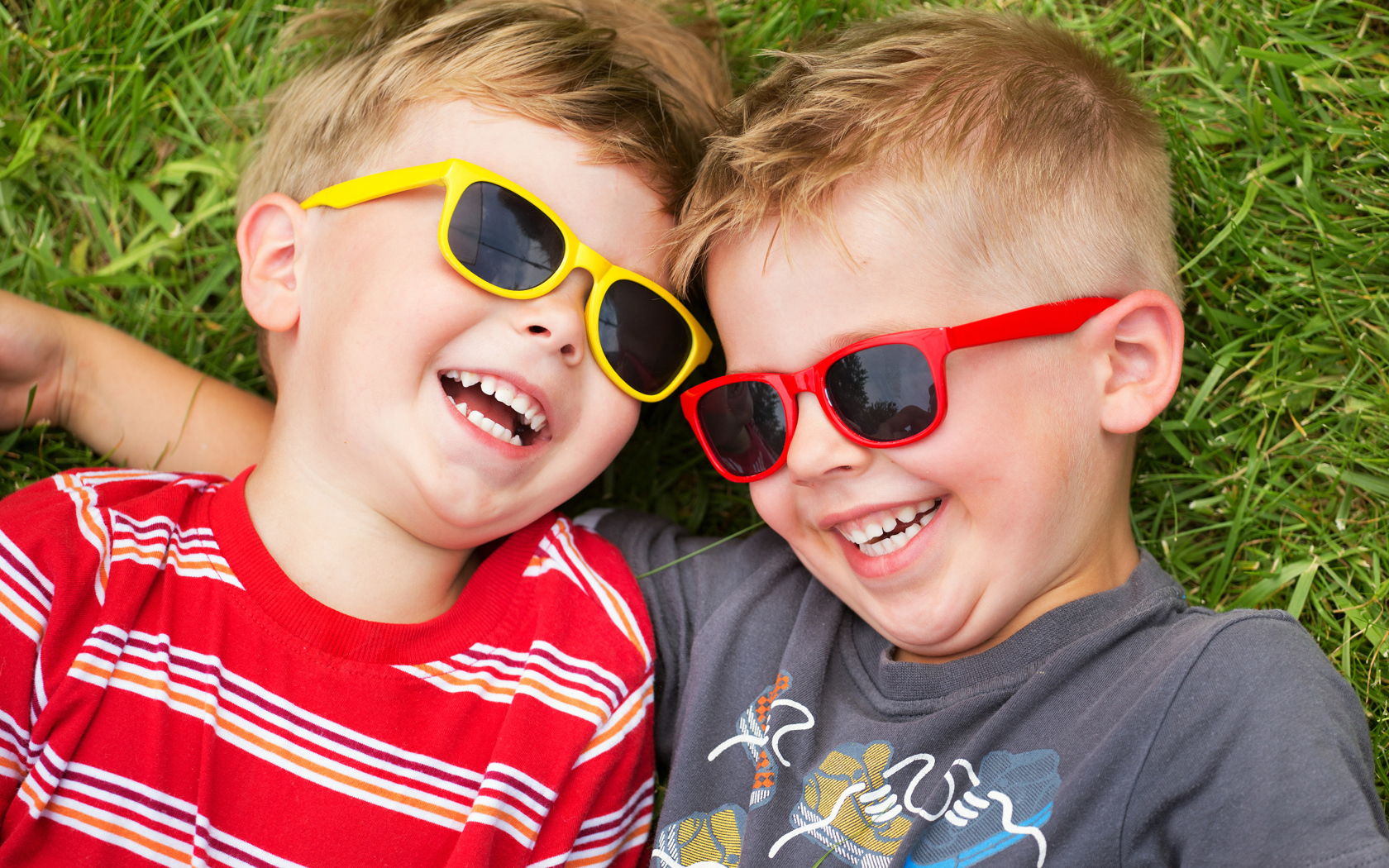 Два улыбающихся мальчика в очках на зеленой траве 