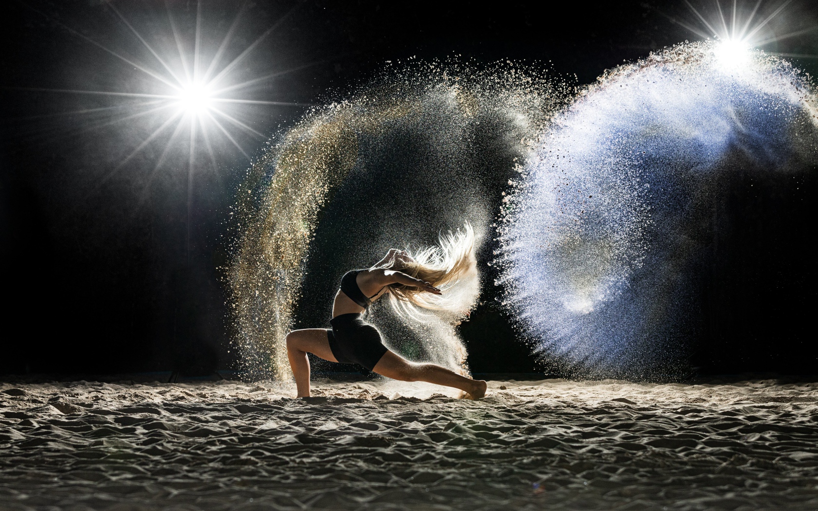 Девушка в черном костюме танцует на песке 