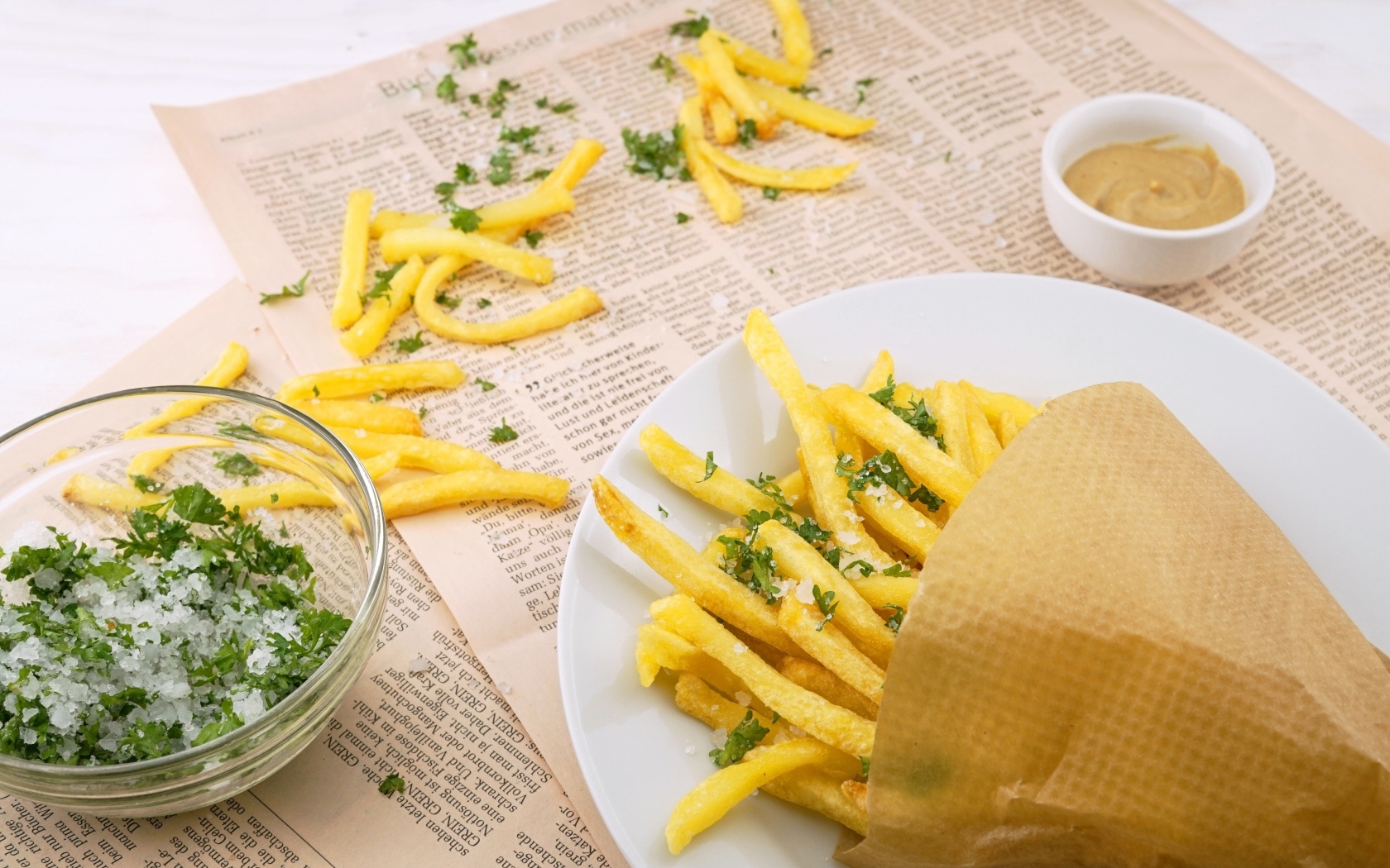 Картофель фри на столе с газетой, солью и зеленью 